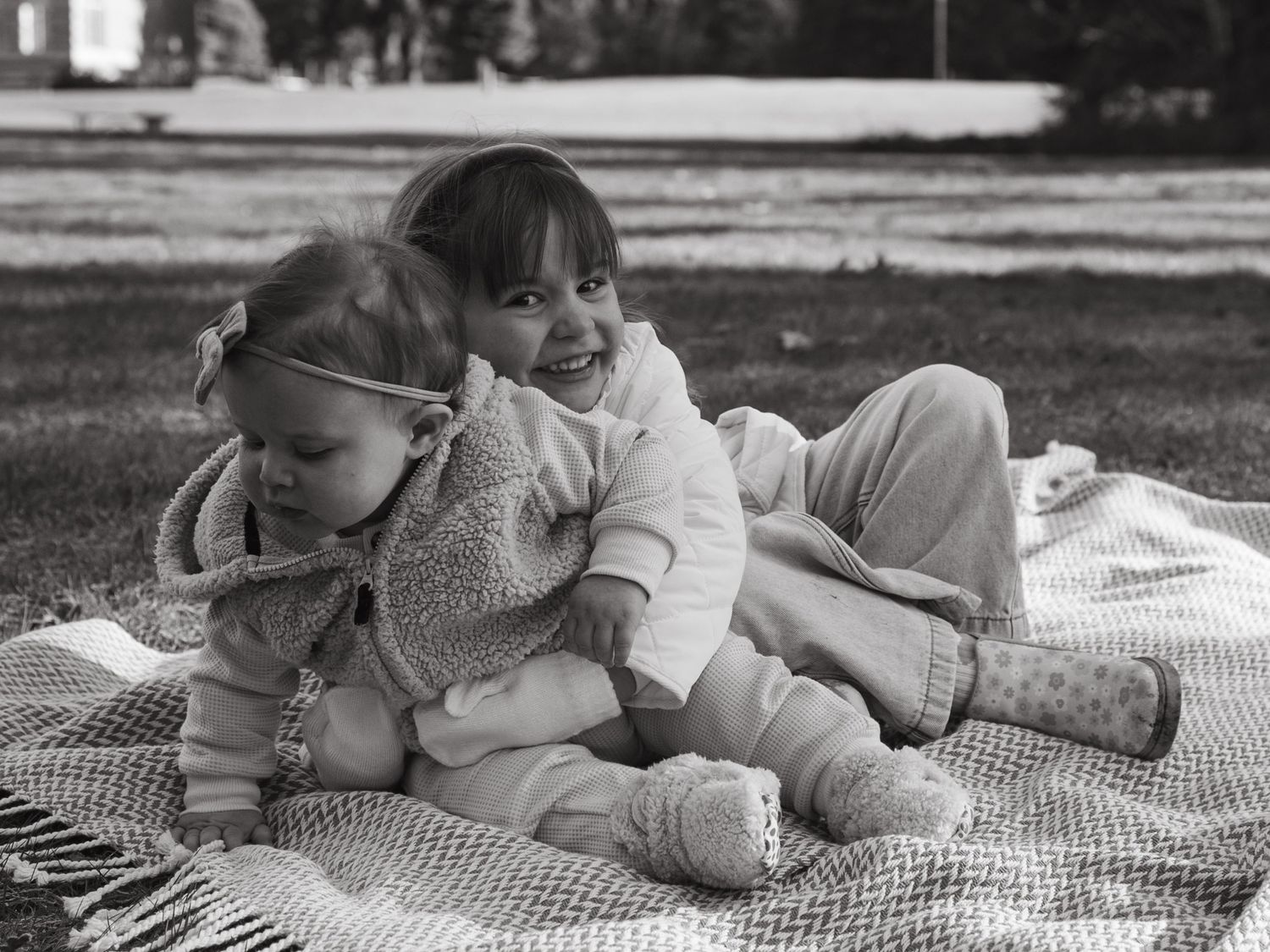 Black and white photo of people relaxing on a checkered blanket outdoors.