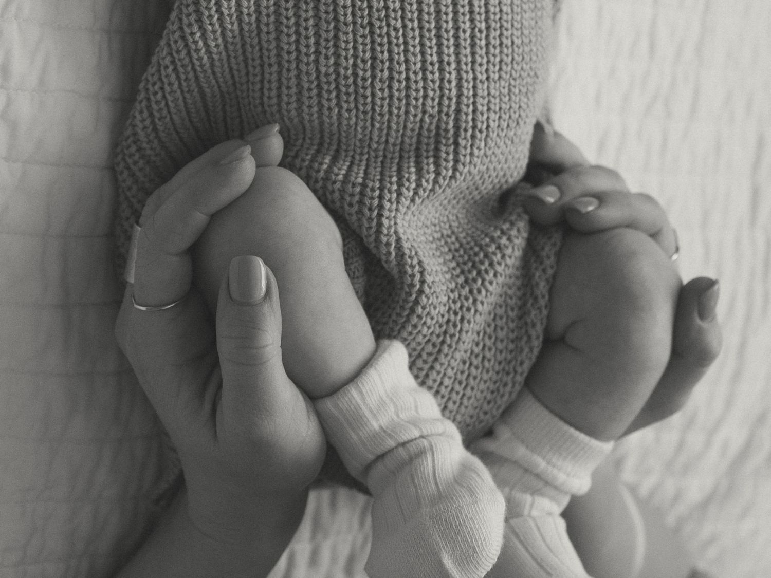 Close-up of tiny baby hands grasping a gray knit sweater in black and white.