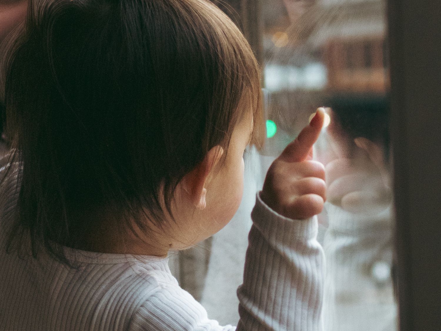 A small child points at something through a window, creating a contemplative scene.