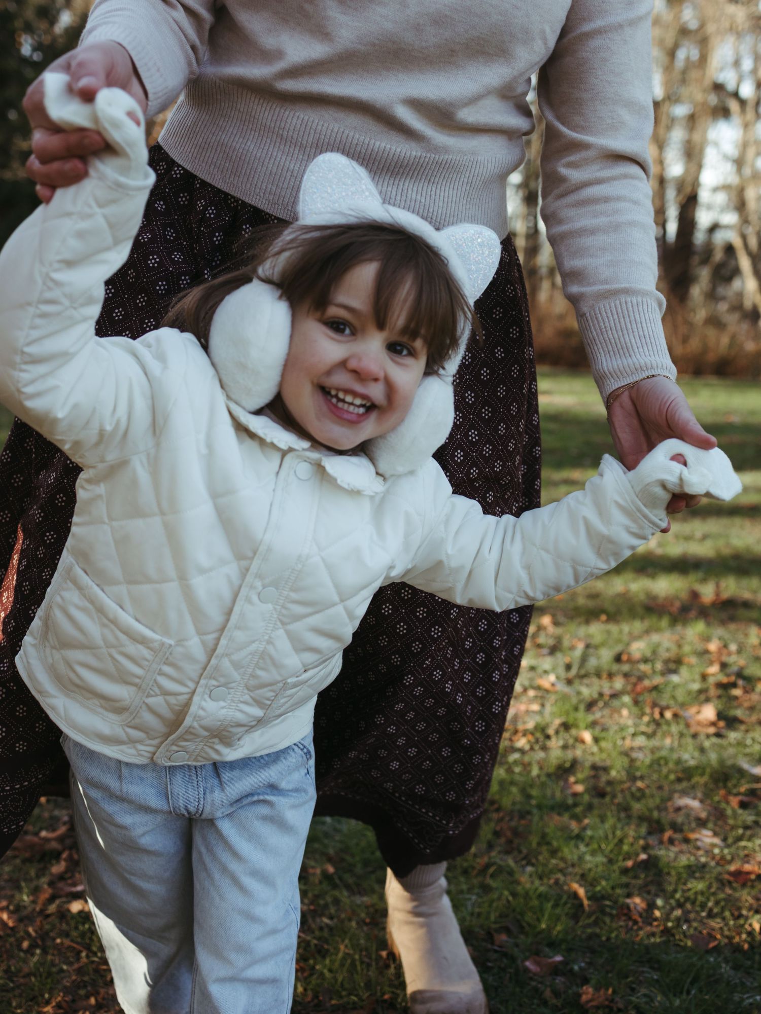 A child in a white winter coat plays outdoors on a fall day.