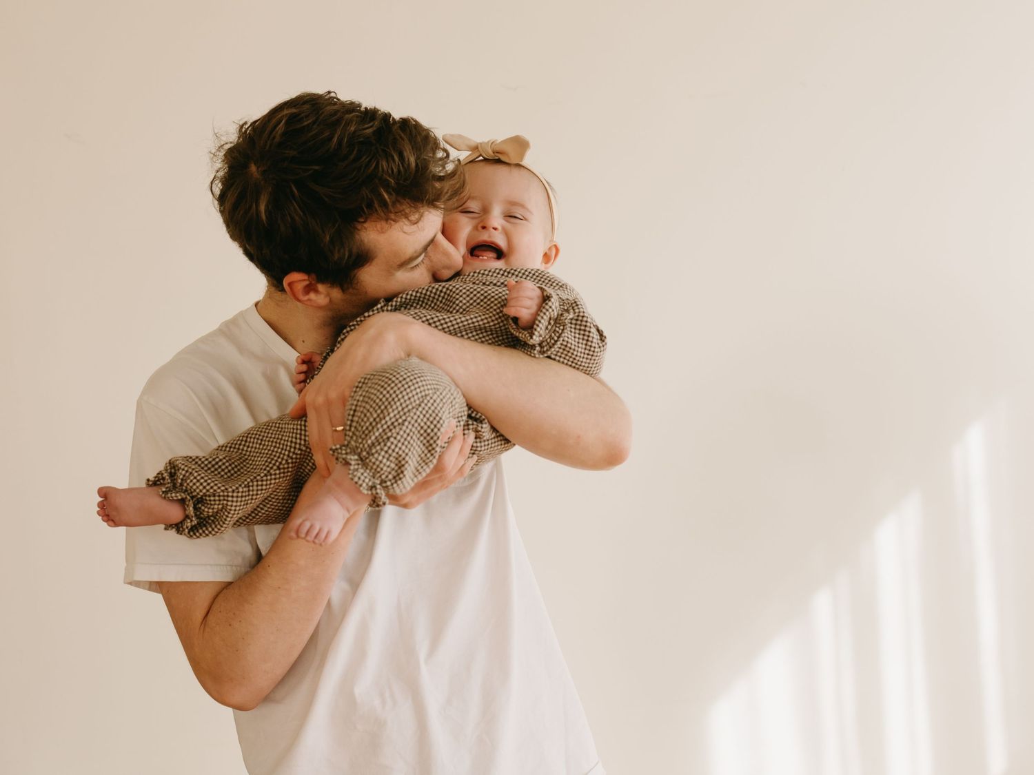 Series of emotional family moments captured against a simple white wall with natural lighting.