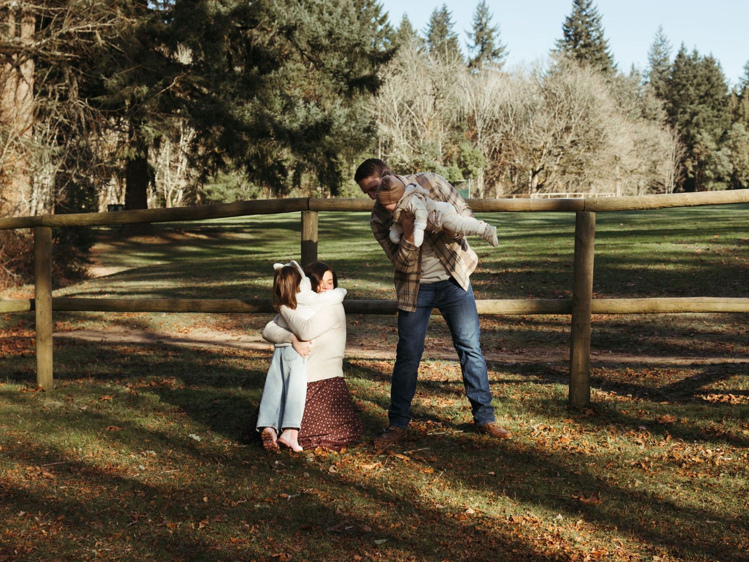 A family shares playful moments together on an autumn day near a wooden fence.