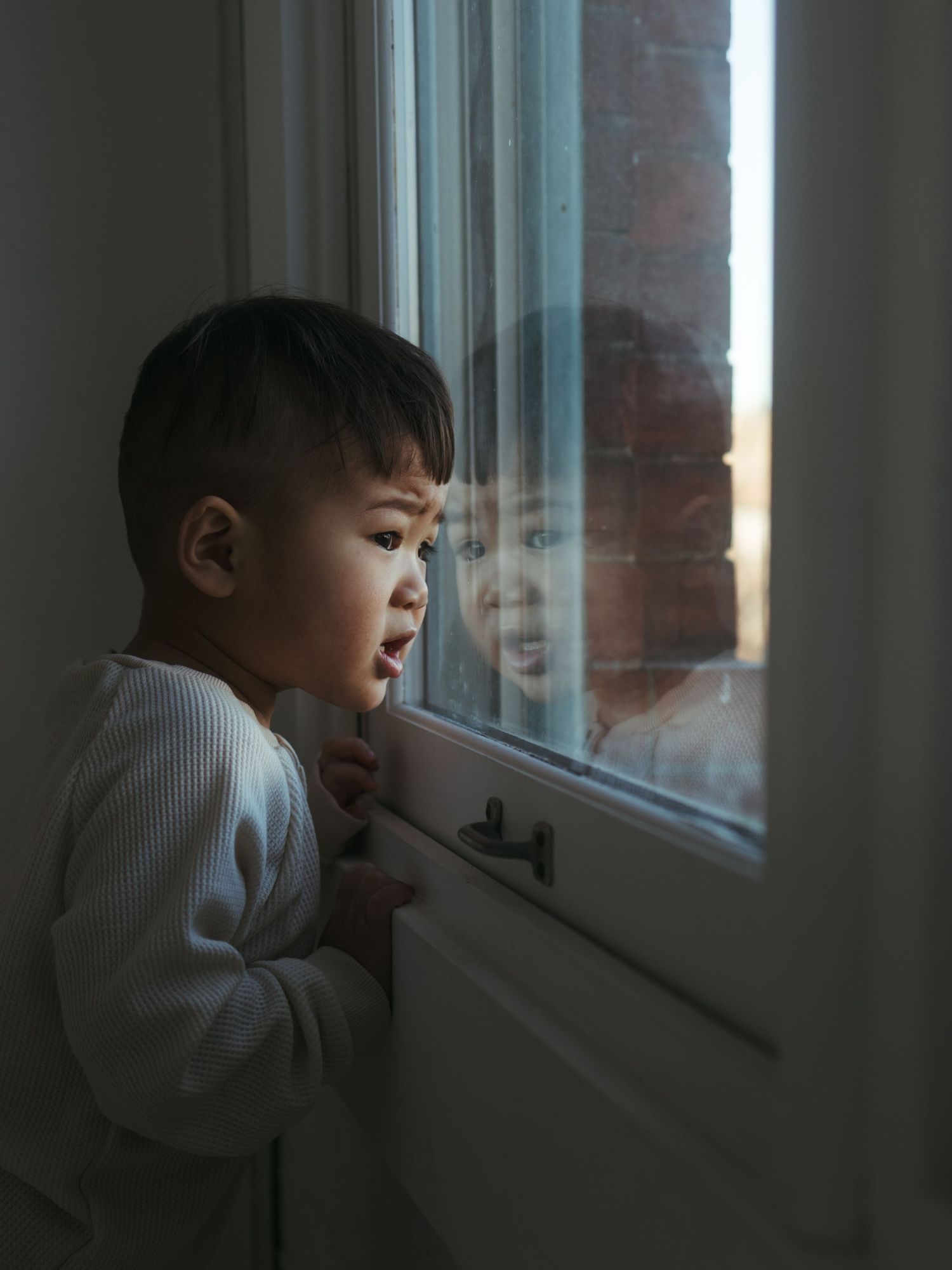 A child looking out of a window in moody natural lighting.