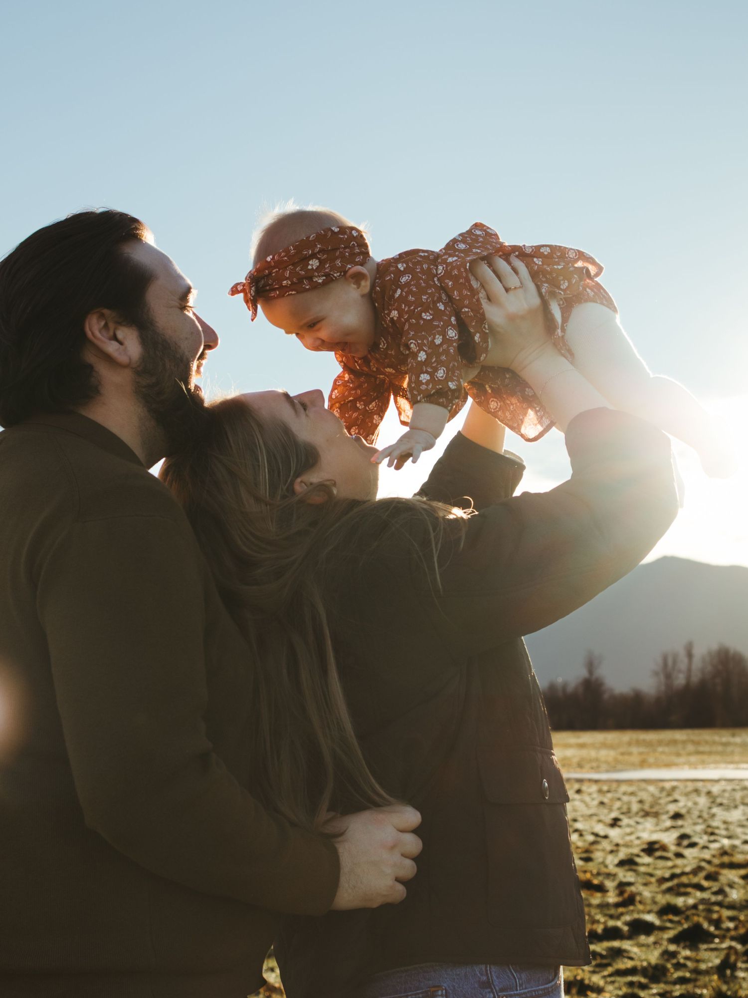 Silhouettes of a couple sharing intimate moments against a bright sunlit backdrop in a field.