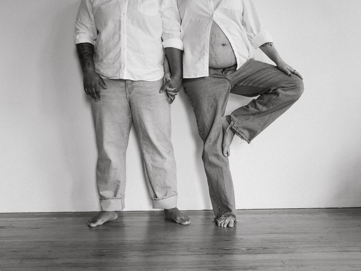 People in white shirts and jeans standing against wall showing only their lower bodies.