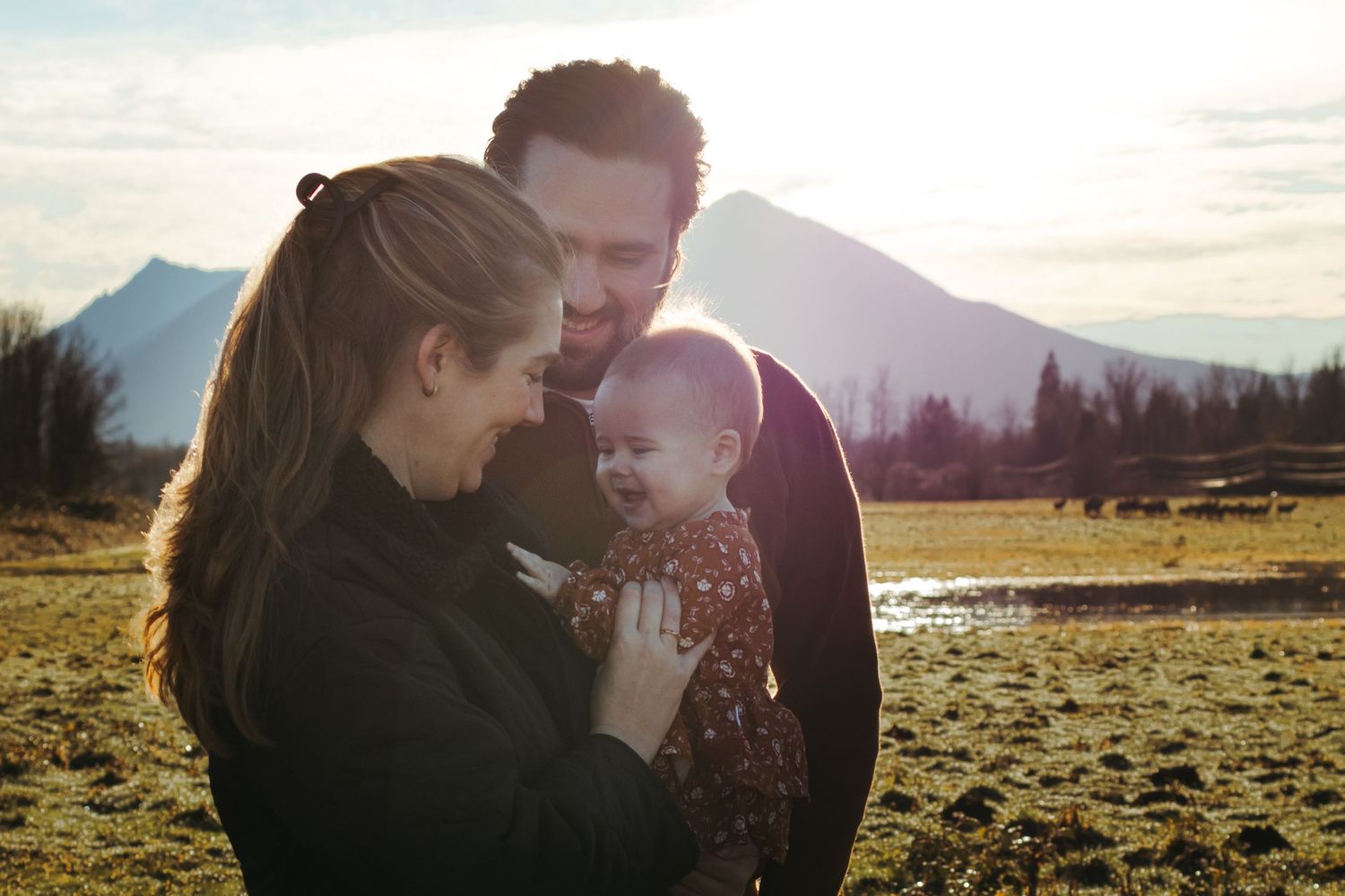 Family sharing an intimate moment in golden sunlight with mountain landscape behind them.