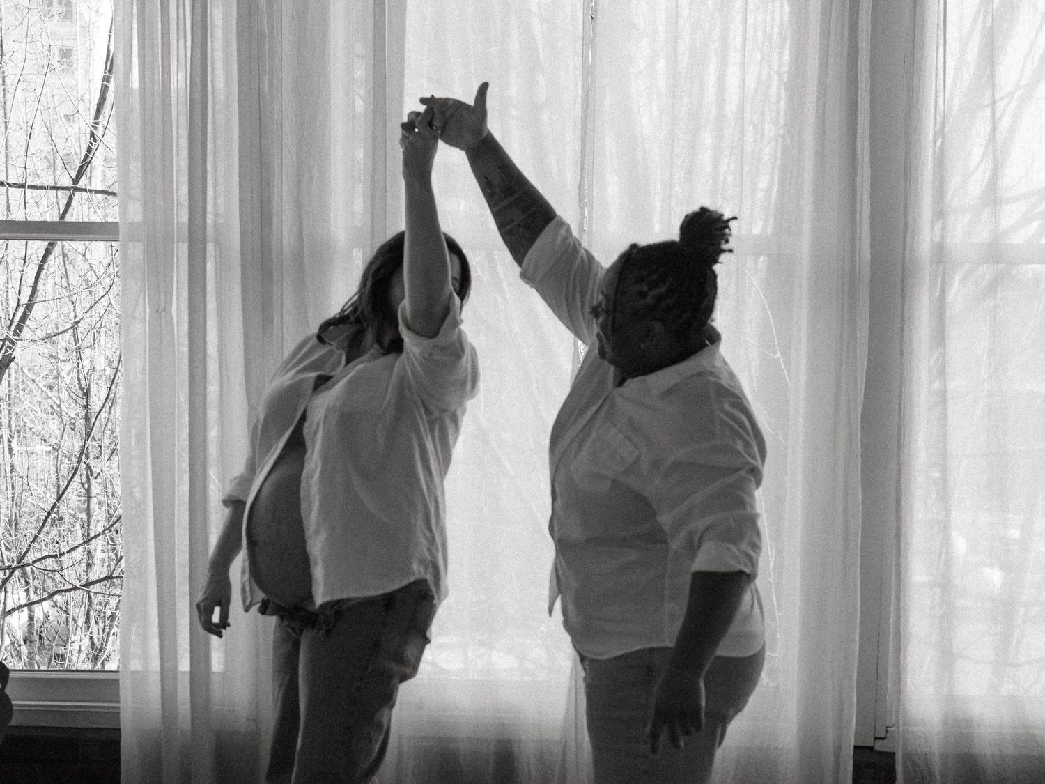 Silhouettes dance and pose against bright window light in artistic black and white composition.