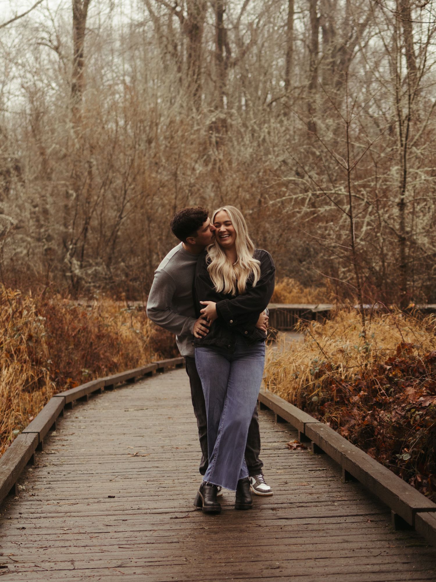 Couple sharing intimate moments on a wooden boardwalk surrounded by fall foliage.
