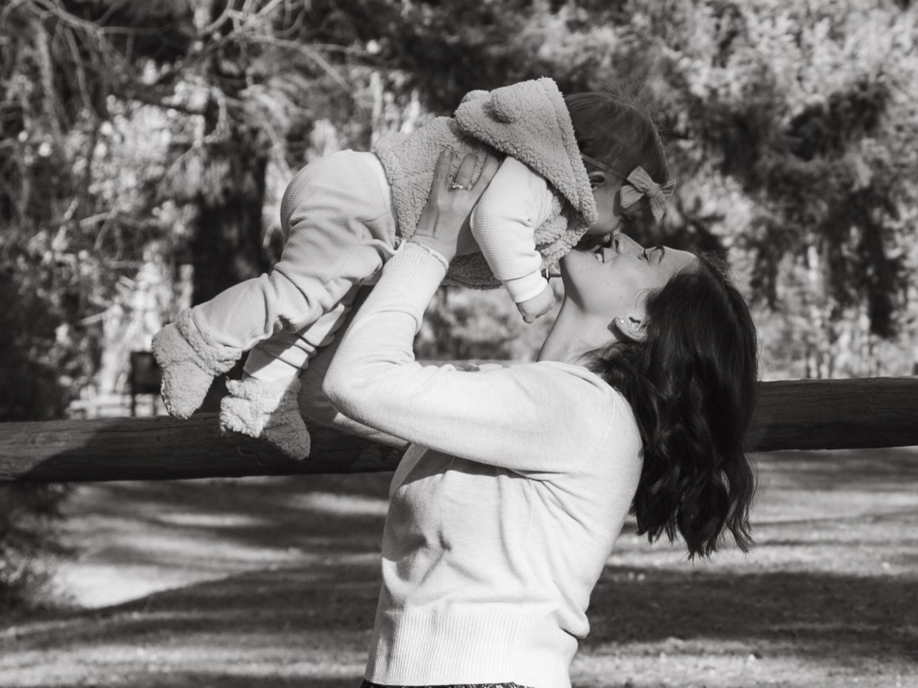 A black and white photo of a joyful outdoor moment lifting a child in a park setting.