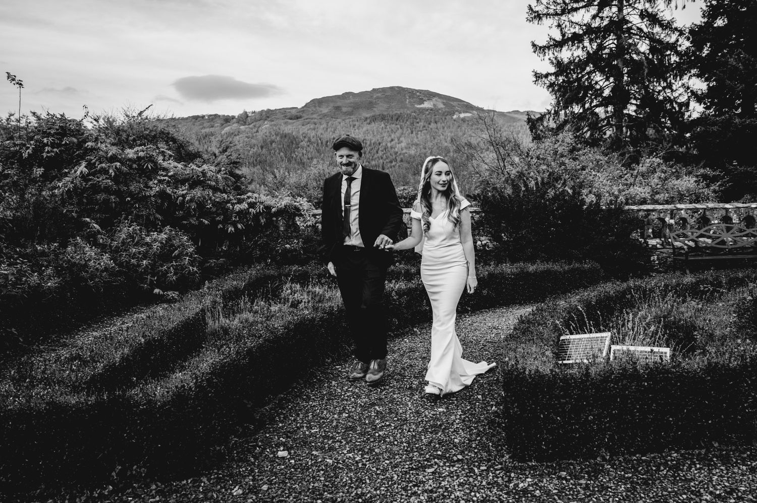 Scenic black and white wedding photo with couple walking along a mountain path.