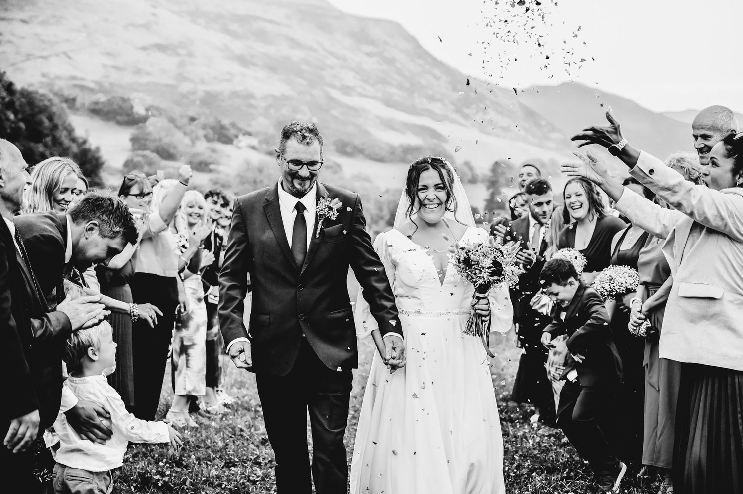 Black and white photo of wedding guests celebrating outdoors with confetti.