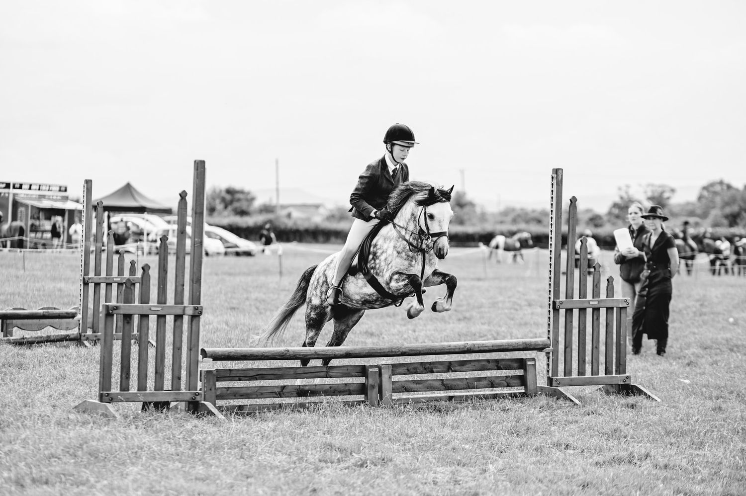 Sequence of black and white photos showing horse and rider clearing jumps at a competition.
