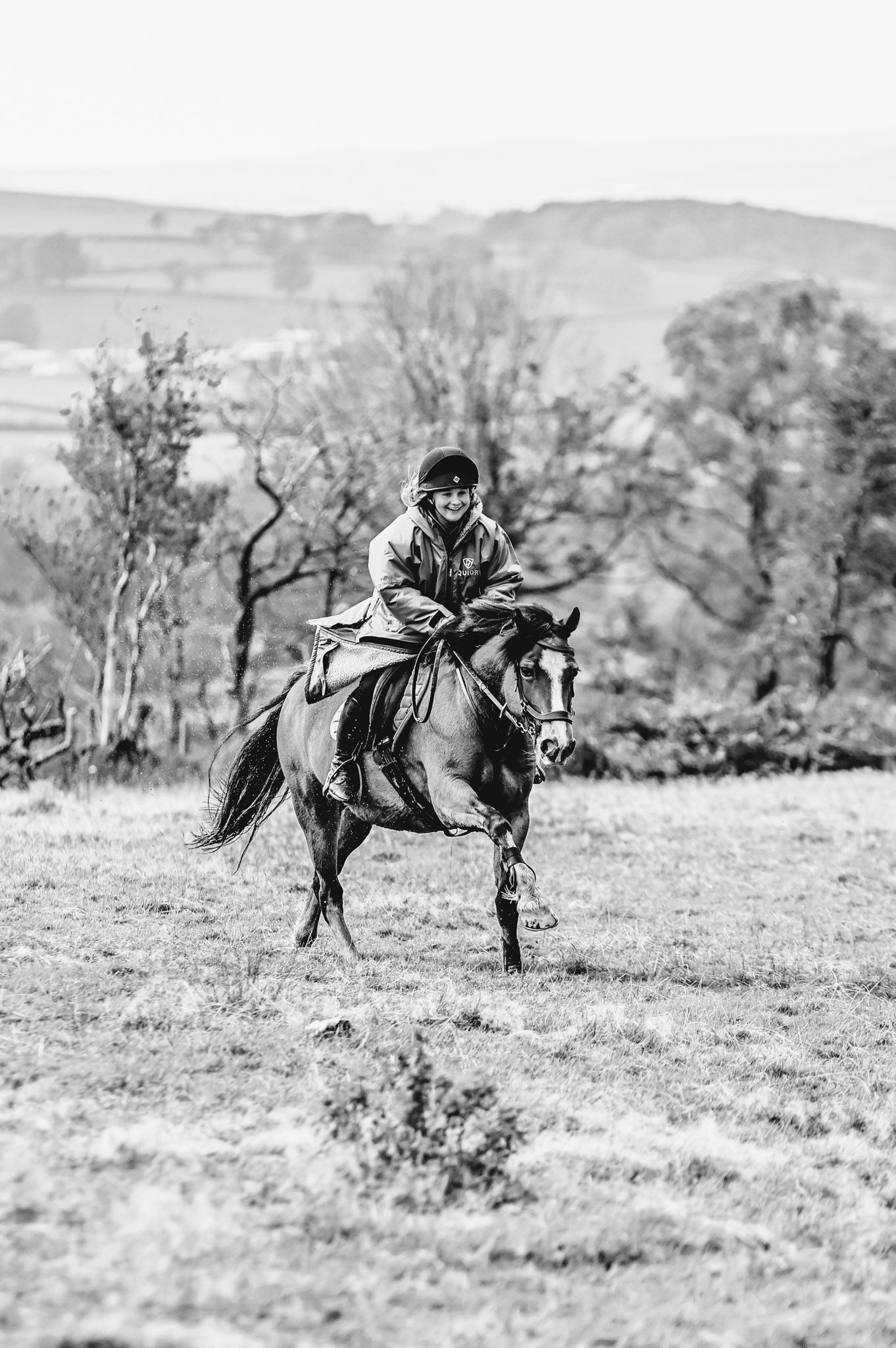Black and white photo of a horse galloping through a grassy field with mountains in the background.