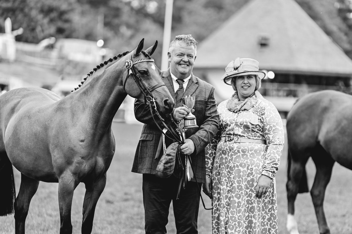 Monochrome image showing horses and handlers arranged in a line at an outdoor competition.