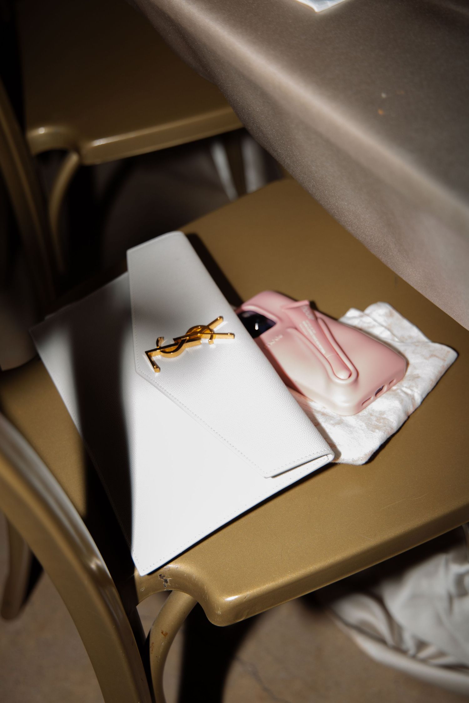 An YSL clutch and pink phone case rest on a gold chair at an elegant wedding reception venue.