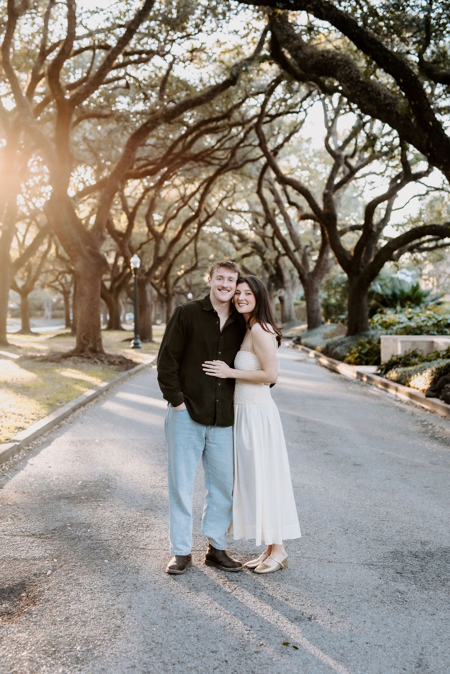 Couple posing on a tree-lined path at golden hour during an engagement photo session.