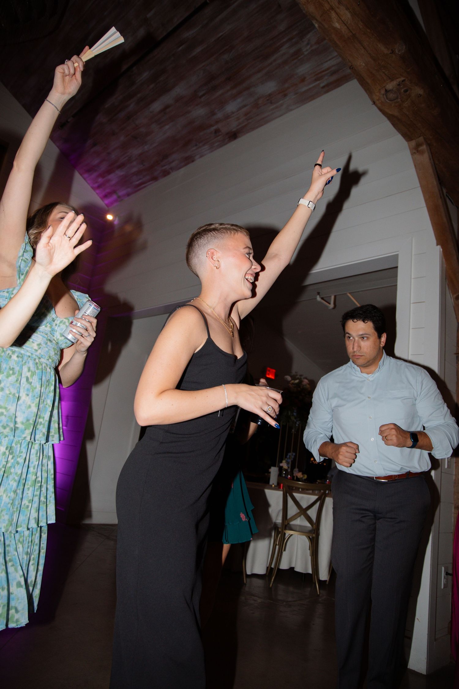 Guests dancing and celebrating at a wedding reception in a rustic barn venue with wooden beam accents.
