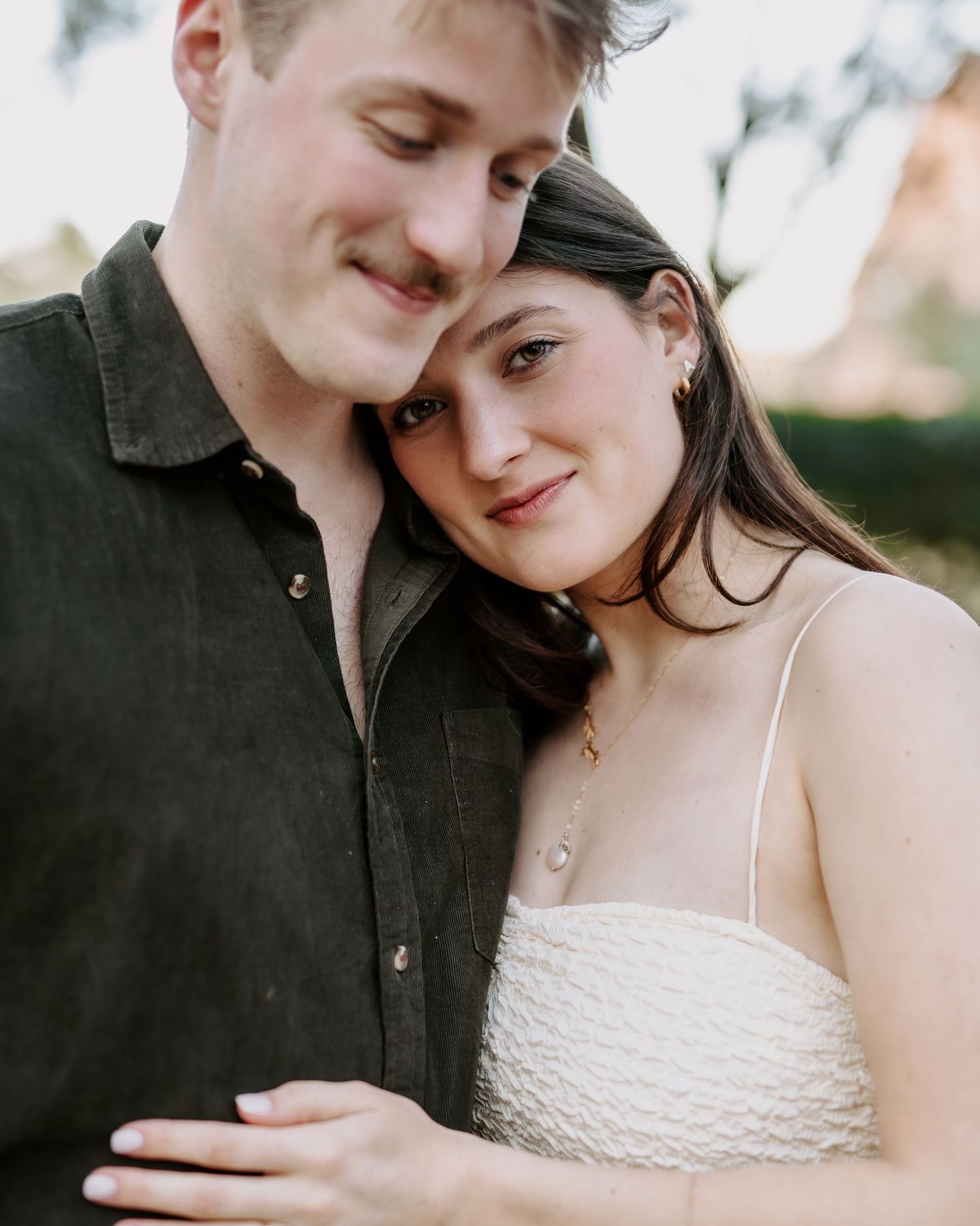 Close-up portrait of an engaged couple embracing tenderly during golden hour outdoors.