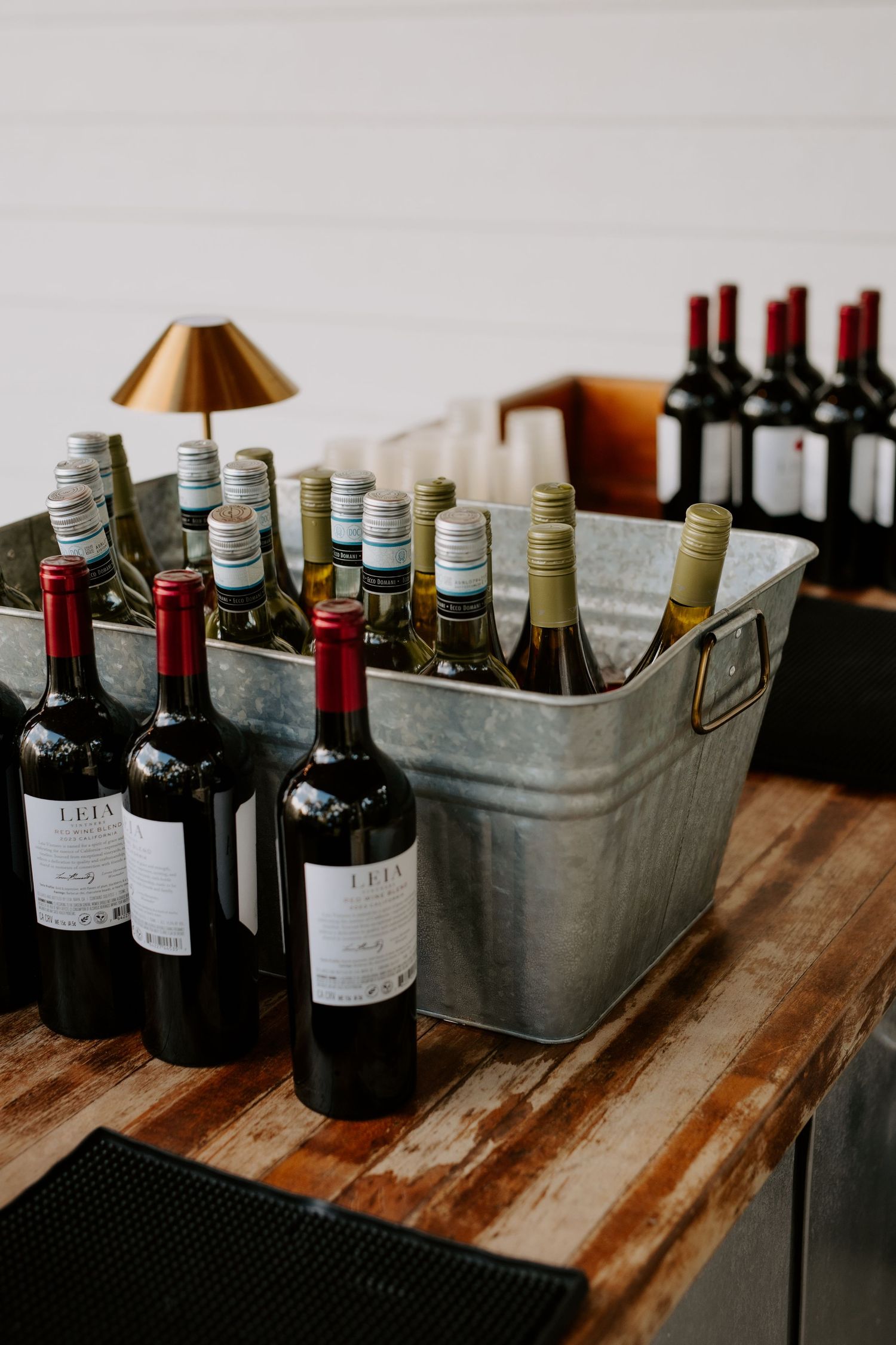 Wine bottles displayed in galvanized metal bucket and wooden table at outdoor wedding bar setup.