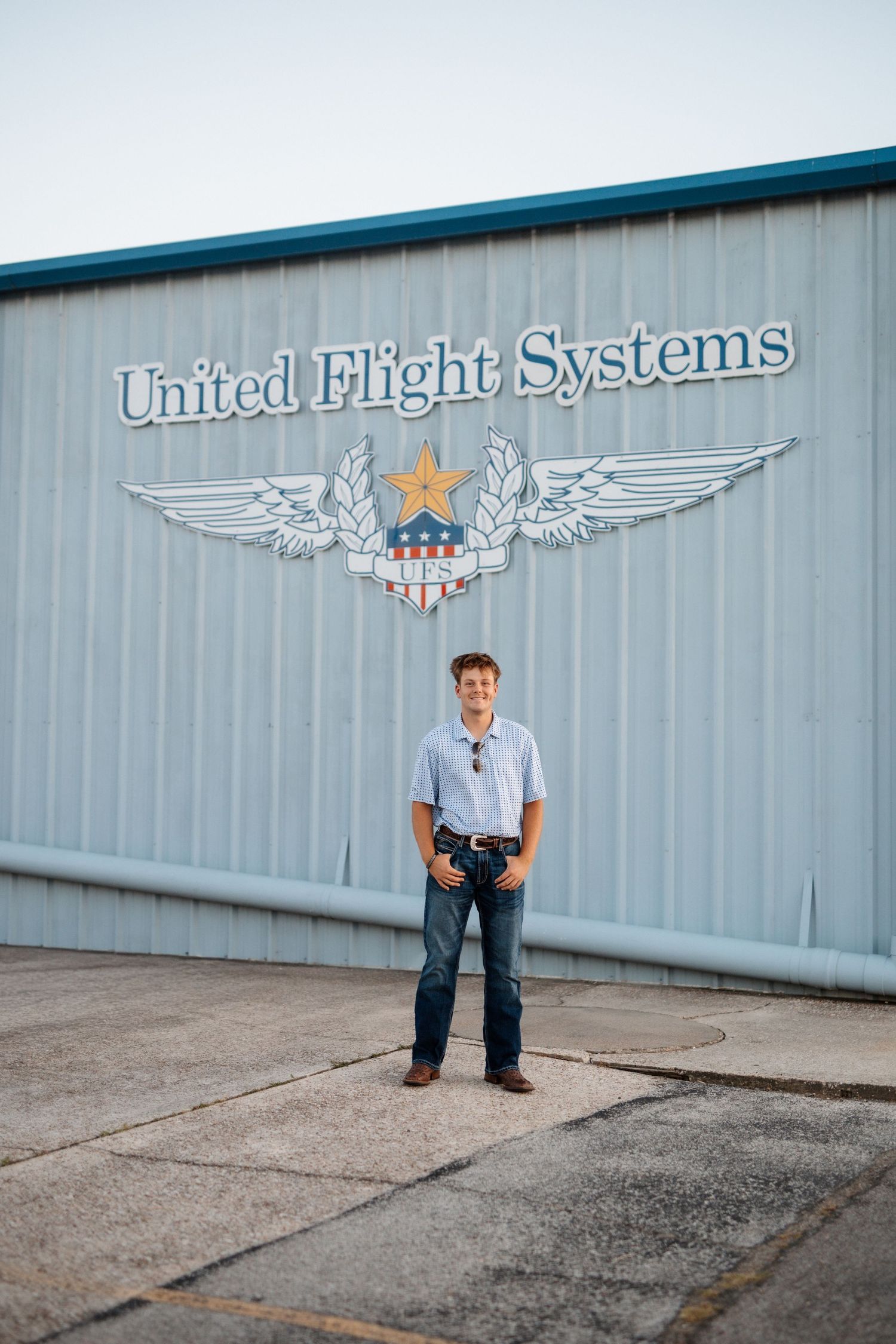Young man standing in front of United Flight Systems aviation hangar building.