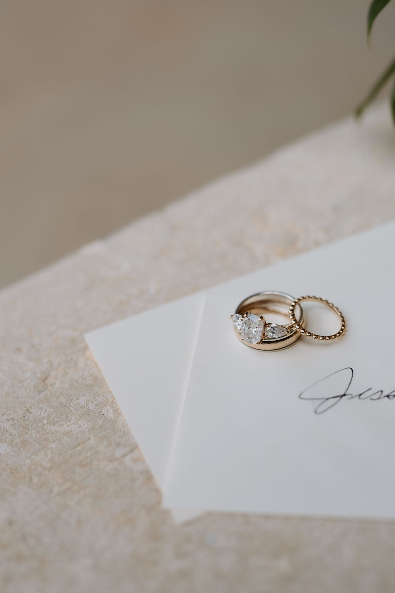 Gold diamond engagement ring and wedding band stacked on a white wedding invitation card.