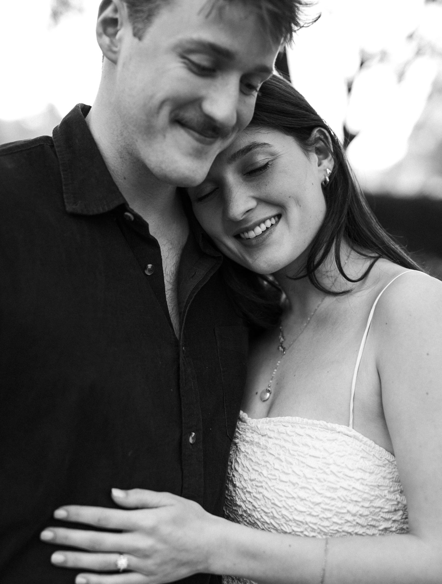 Black and white close-up of a smiling couple embracing during an outdoor engagement session.