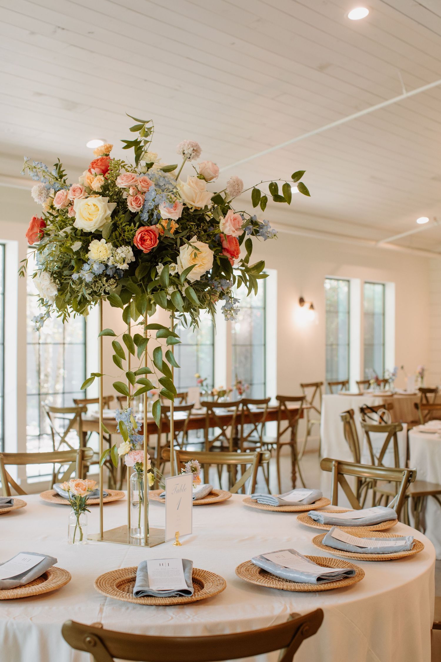 Elegant wedding reception table with tall floral centerpiece of pink, peach, and blue blooms.