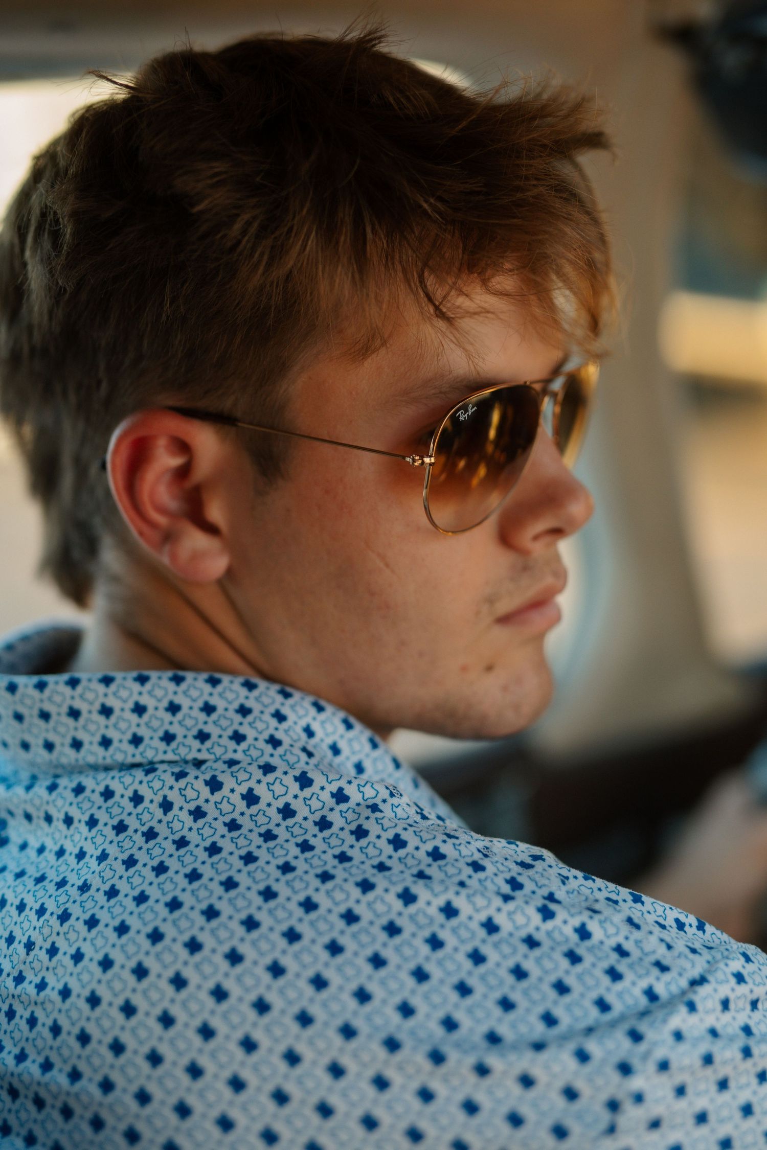 Side profile portrait of a young male pilot wearing aviator sunglasses inside a small aircraft cabin.