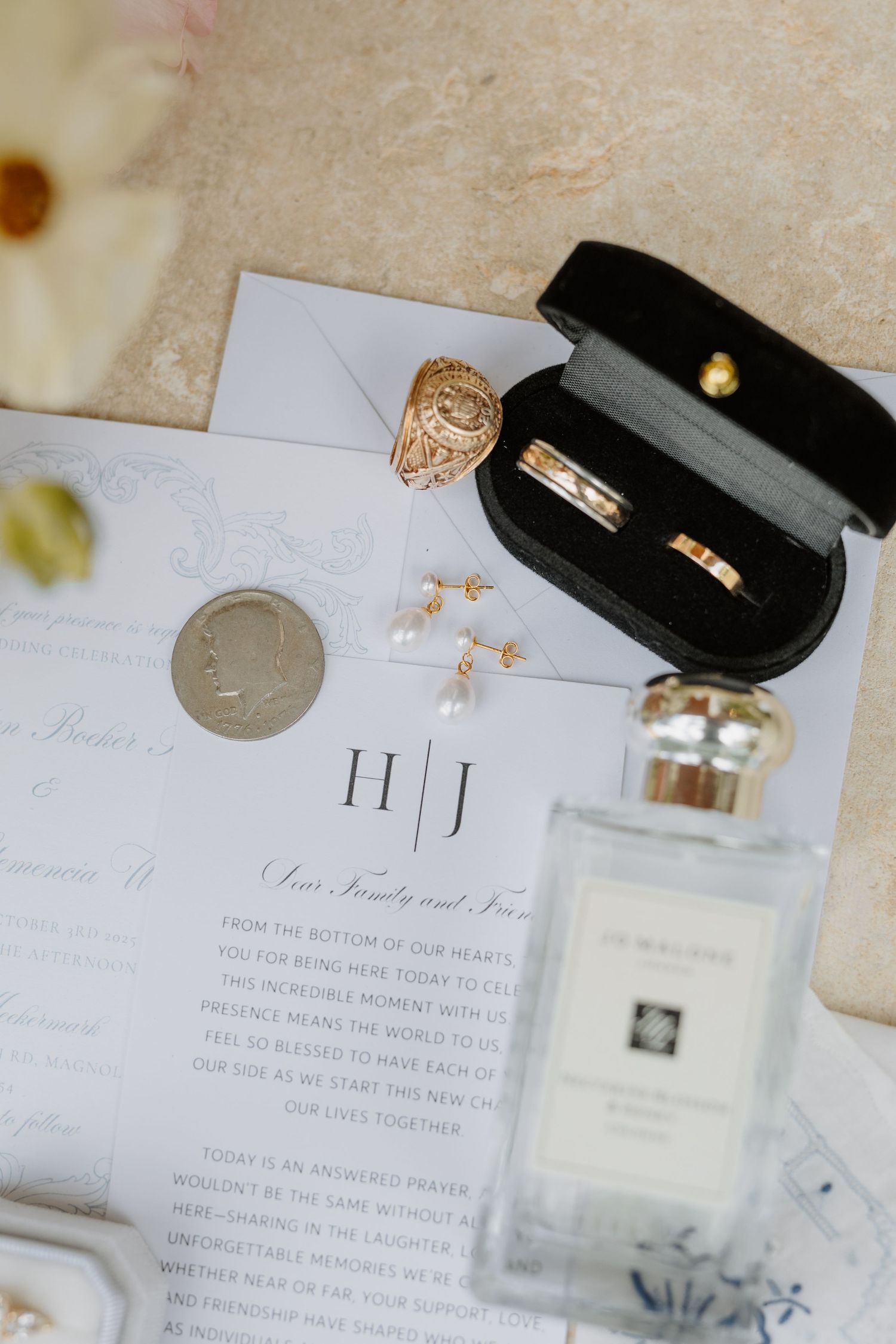 Wedding flat lay featuring gold rings in velvet box, pearl earrings, invitations, and Jo Malone perfume.