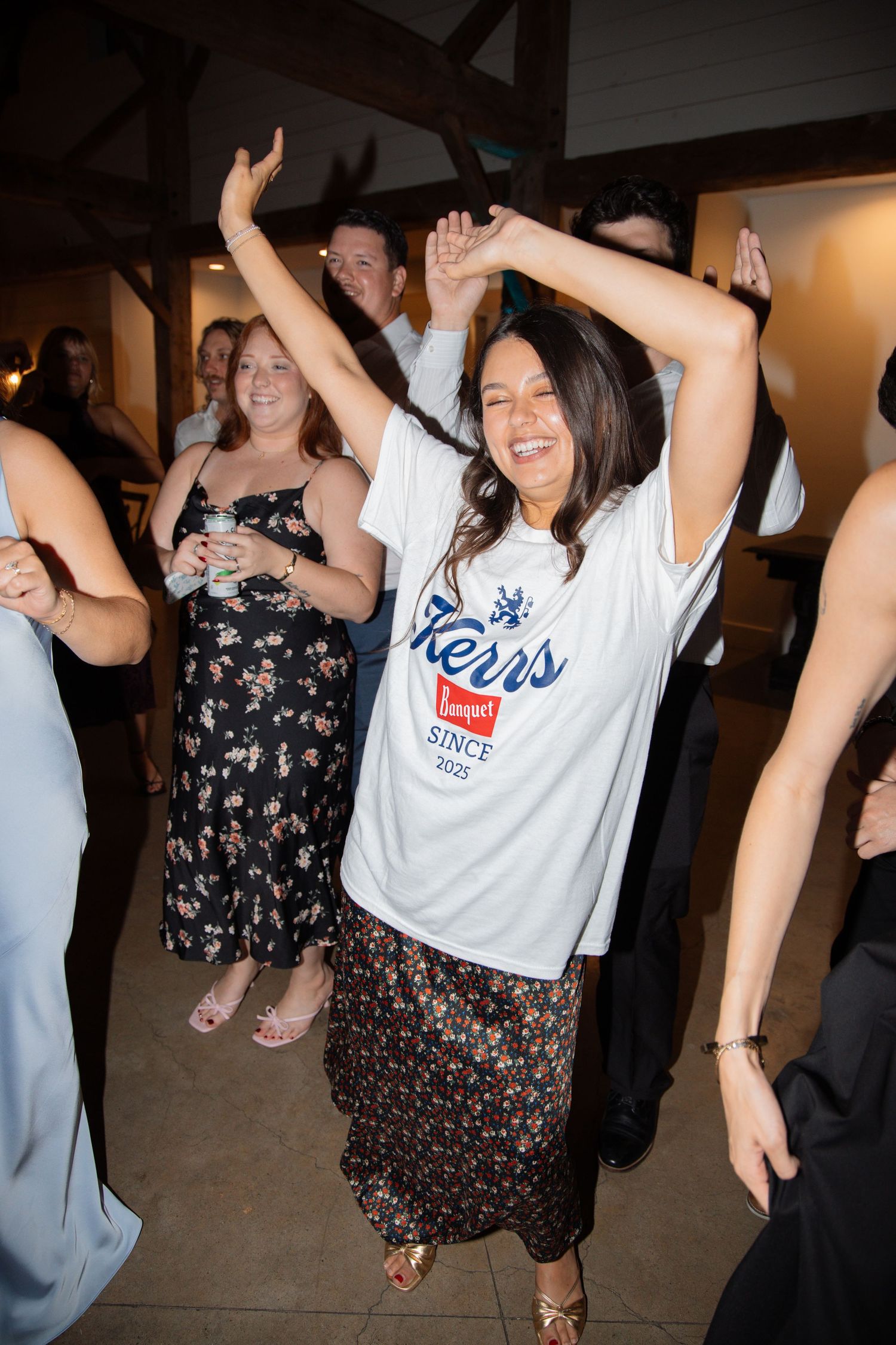 A joyful wedding guest dances with arms raised wearing a Kerrs since 2025 custom t-shirt at a reception.