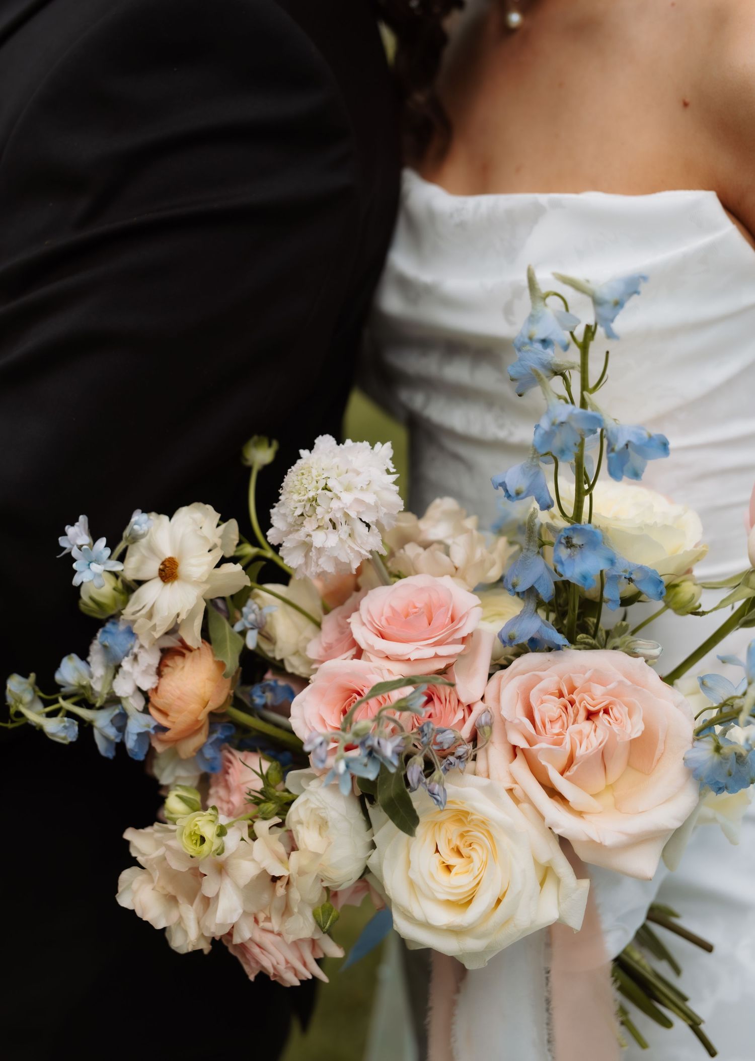 Close-up of bridal bouquet featuring pink roses, blue delphiniums, and white blooms.