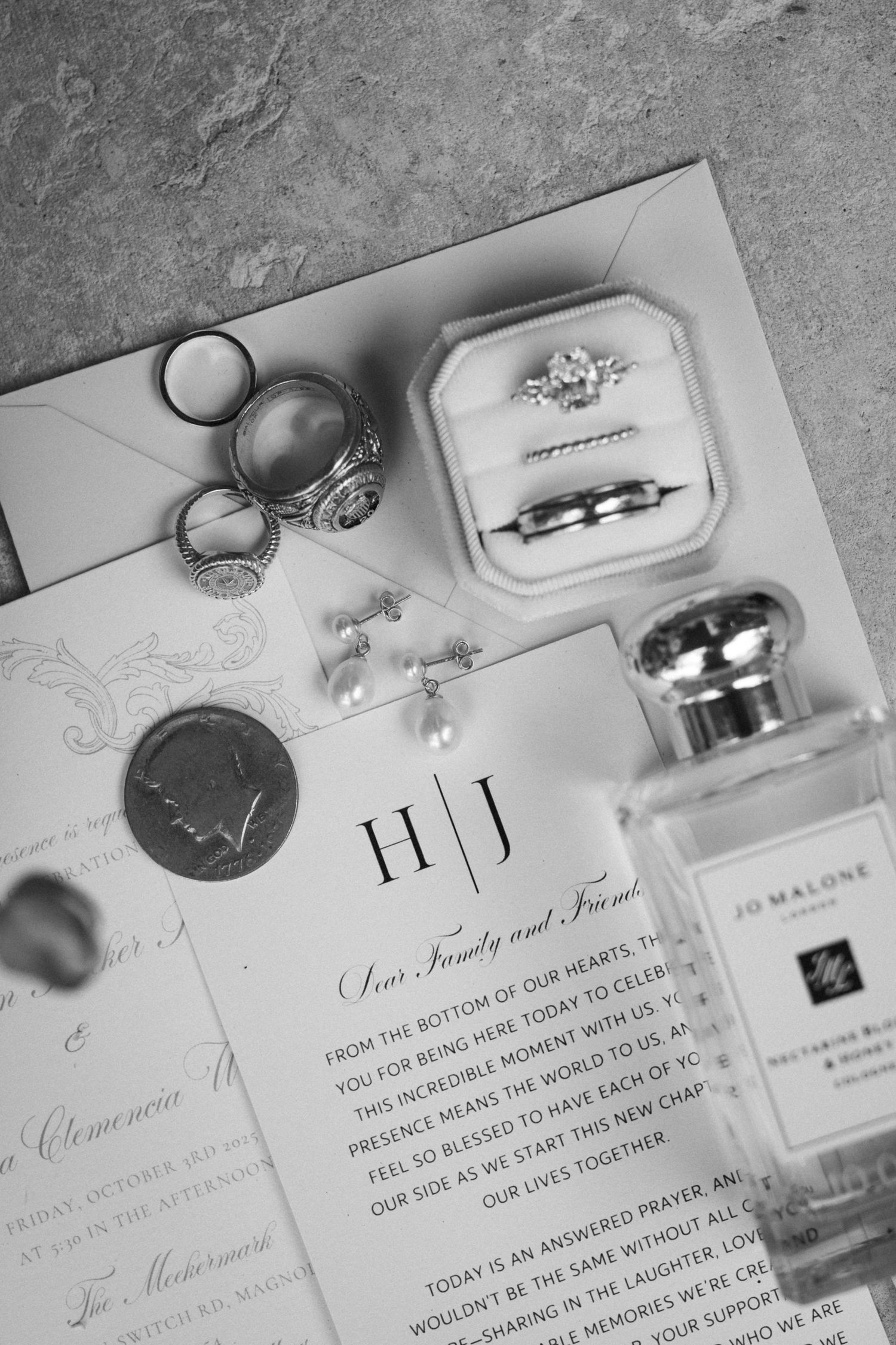 Black and white wedding detail flat lay with diamond engagement ring, bands, invitations, and perfume bottle.
