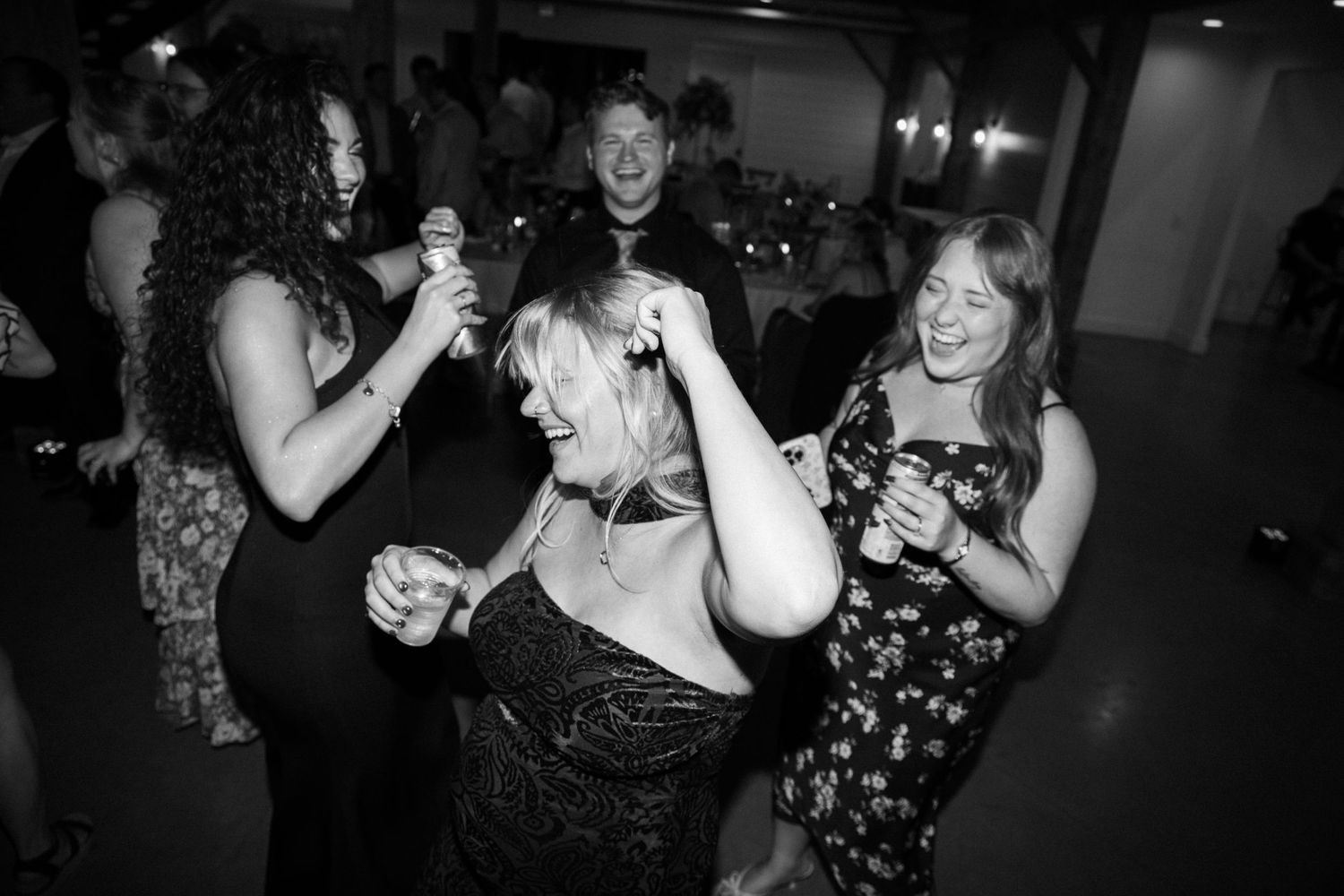 Black and white photo of women dancing and laughing joyfully at wedding reception party.