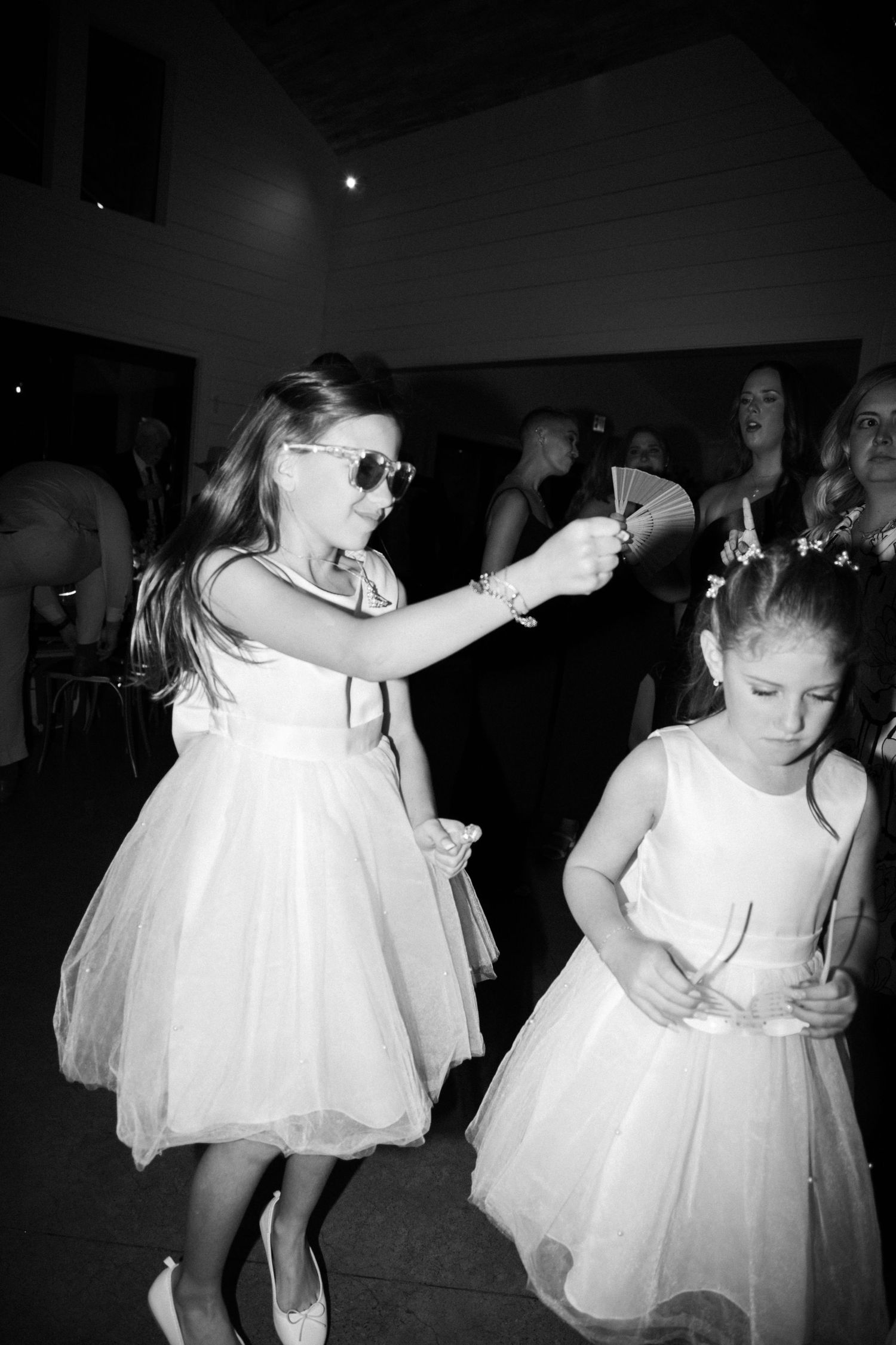 Black and white photo of flower girls in white dresses dancing at wedding reception.