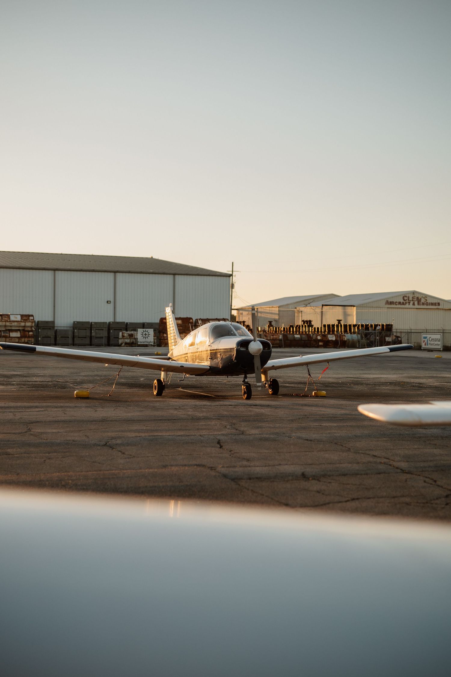 Small single-engine propeller aircraft parked on an airport tarmac at golden hour with hangars in background.
