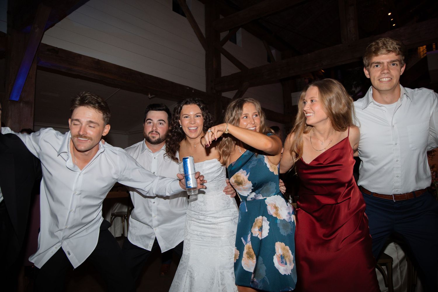Happy wedding party group posing together on the dance floor at a barn wedding reception.