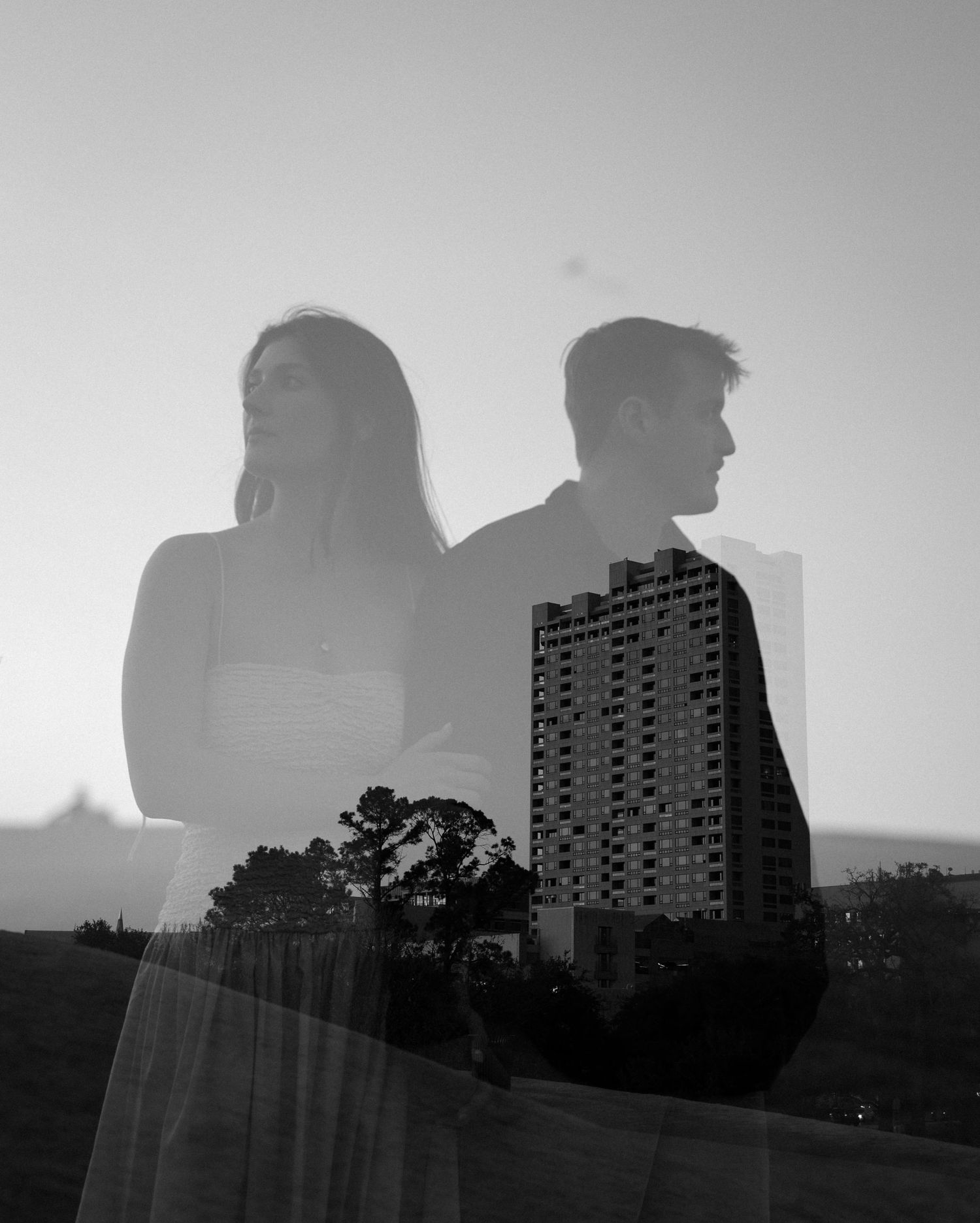 Black and white double exposure portrait of couple silhouetted against city skyline at dusk.