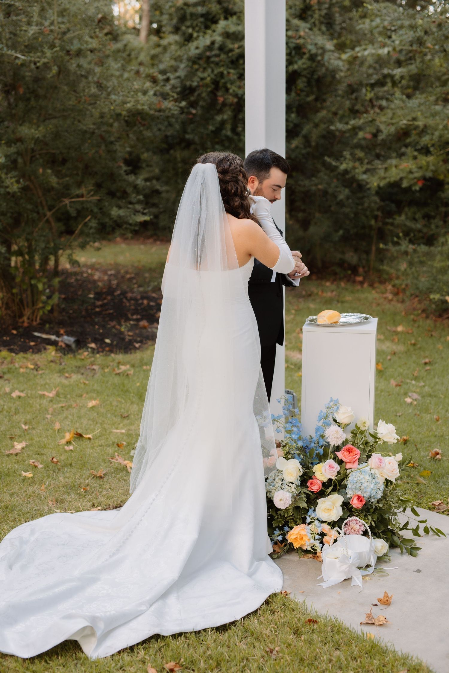Bride and groom perform a unity ceremony at outdoor altar decorated with colorful floral arrangements.