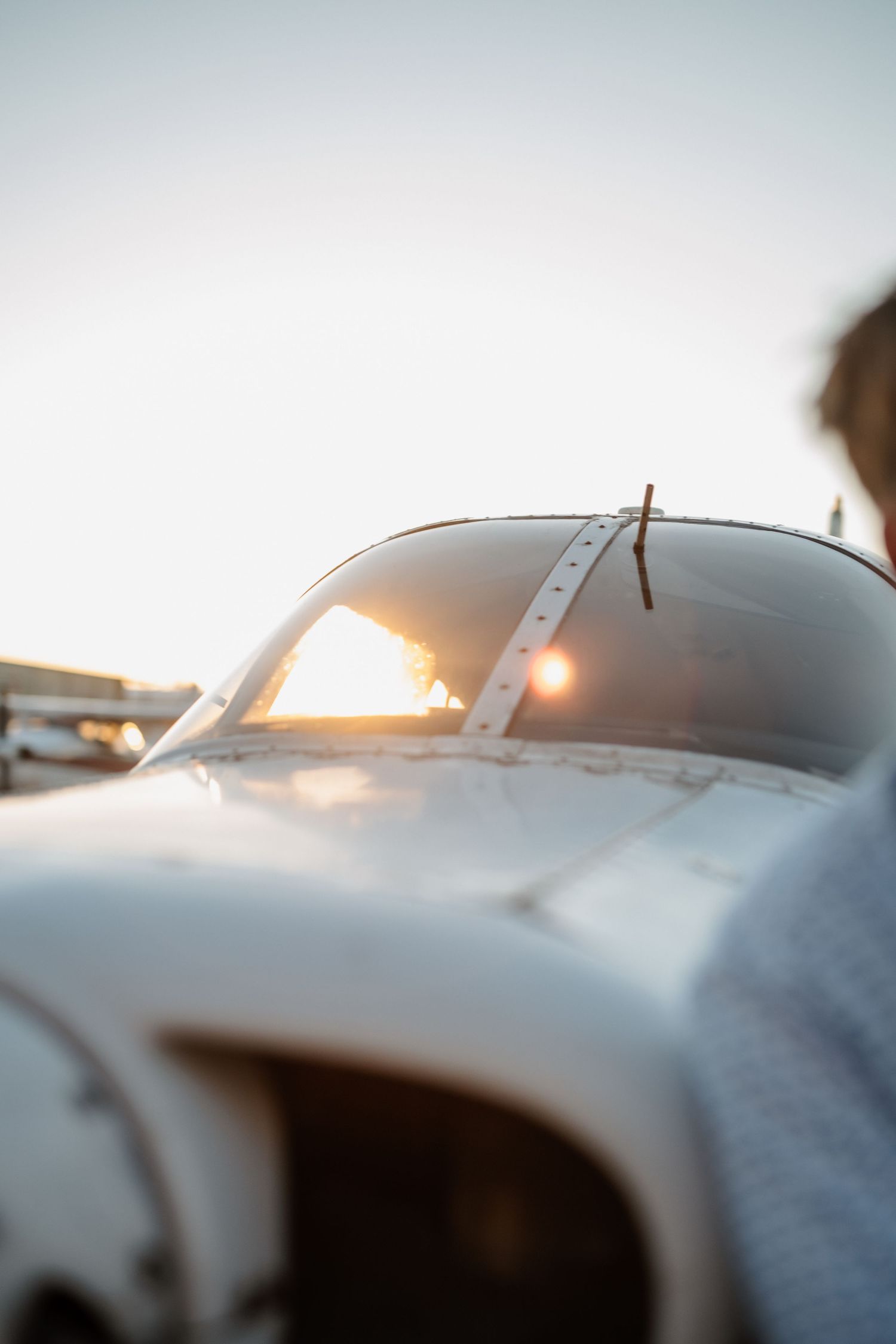 Close-up of a small aircraft canopy reflecting golden sunset light on an airport tarmac.