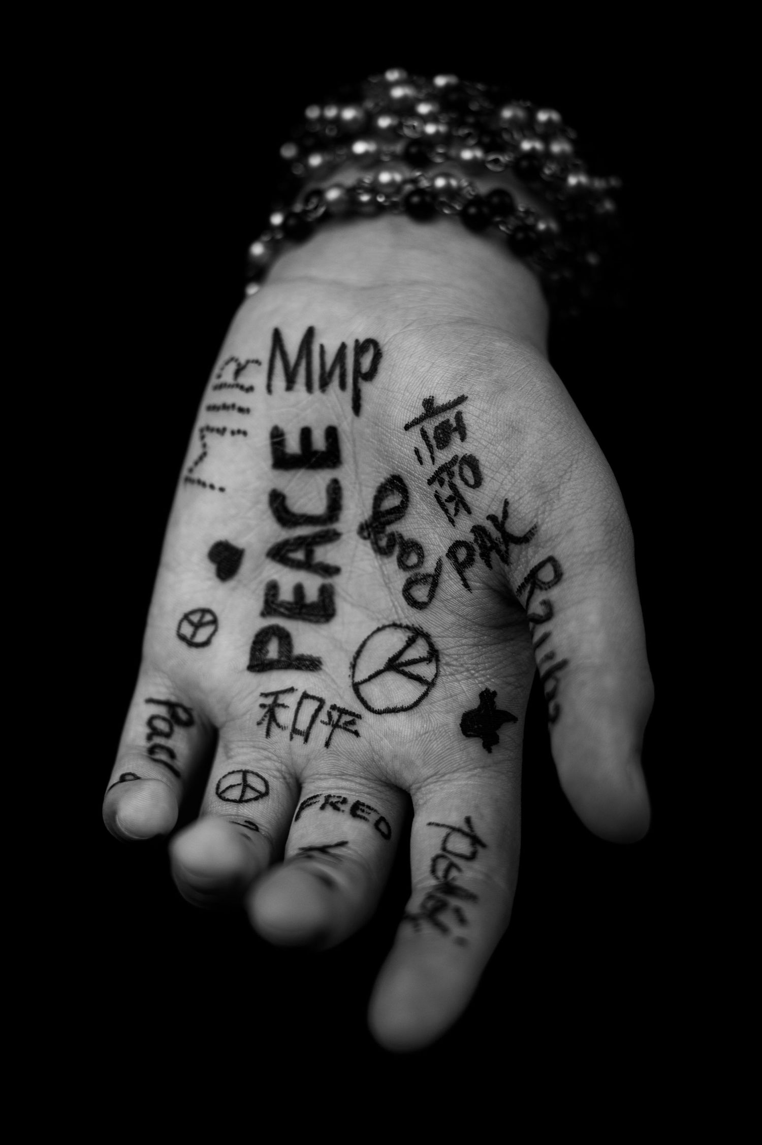 Black and white photograph of a hand with handwritten word peace and symbols drawn in ink on the palms.