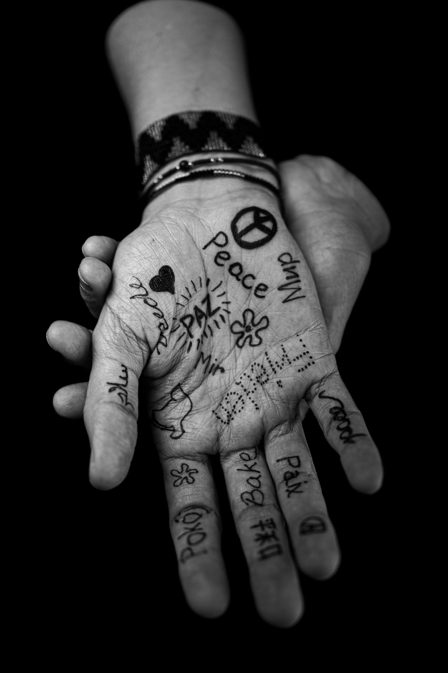 Black and white photograph of a hand with handwritten word peace and symbols drawn in ink on the palms.
