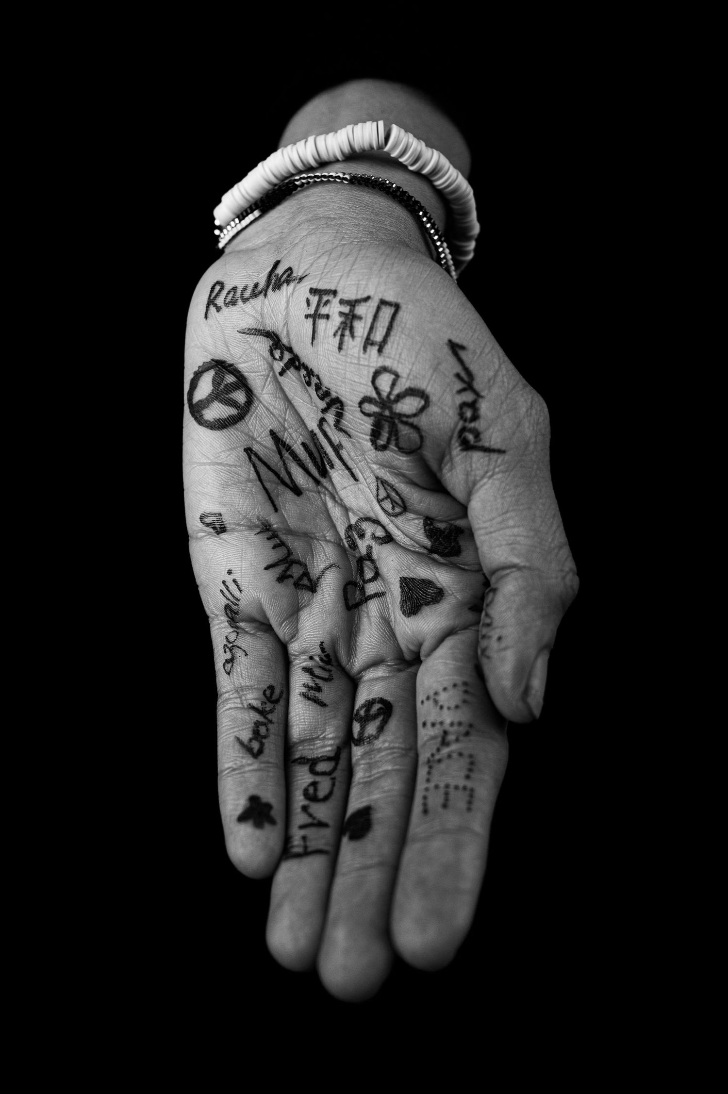 Black and white photograph of a hand with handwritten word peace and symbols drawn in ink on the palms.