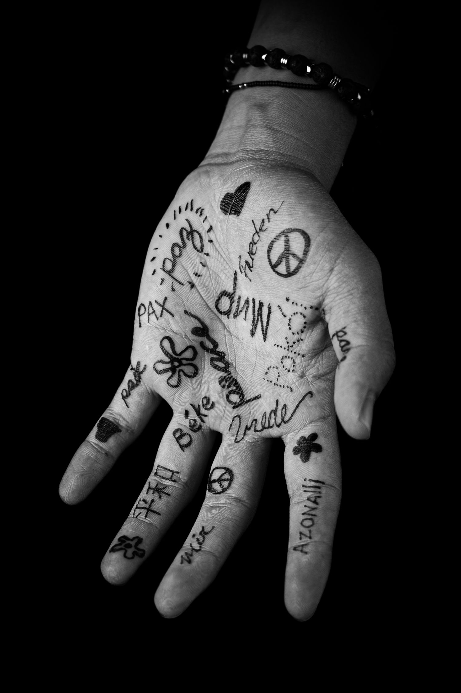 Black and white photograph of a hand with handwritten word peace and symbols drawn in ink on the palms.