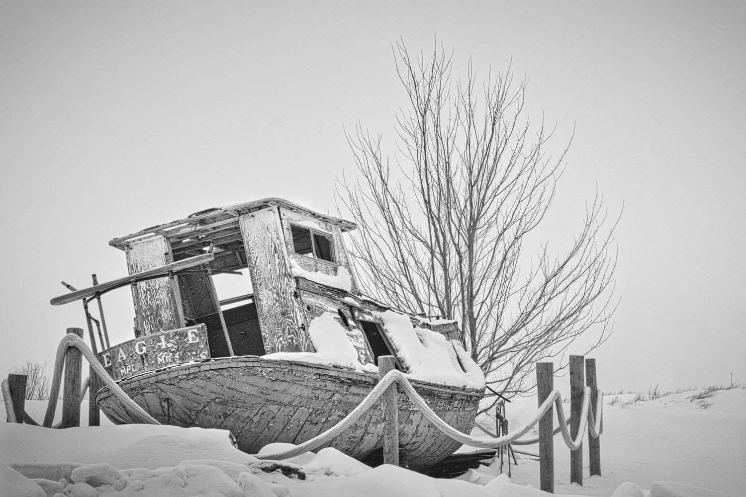 Abandoned commercial fishing boat covered in snow along a winter shoreline in Northern Wisconsin, captured in black and white.