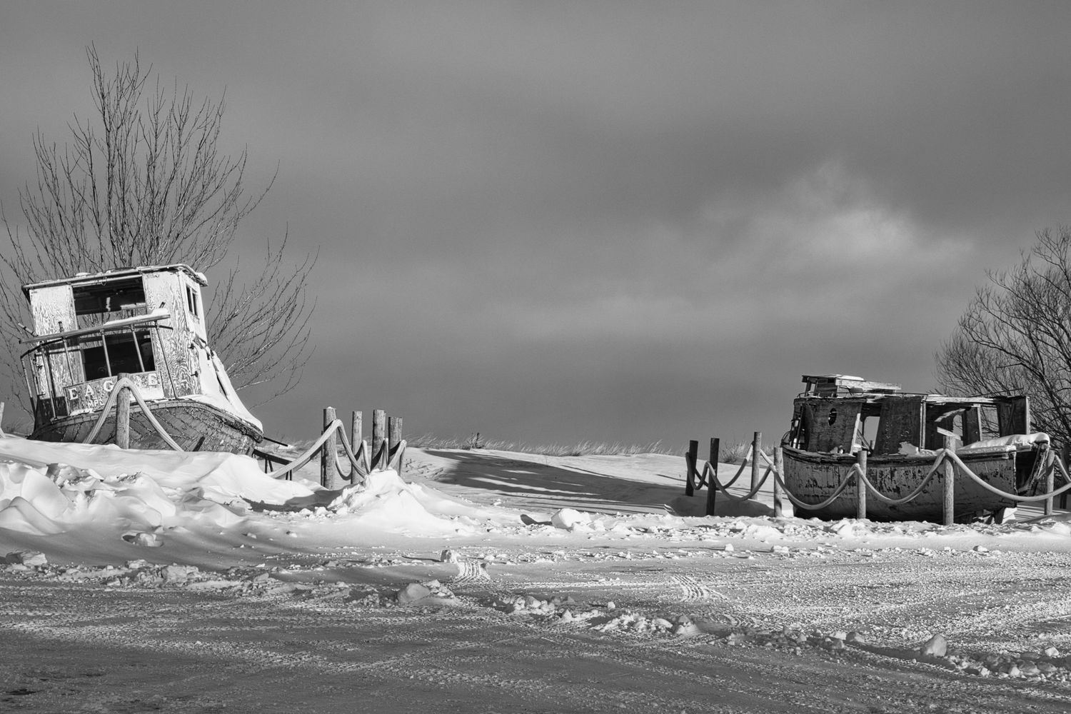 Snow-covered harbor with abandoned commercial fishing boats under a dramatic winter sky in Northern Wisconsin, captured in black and white.