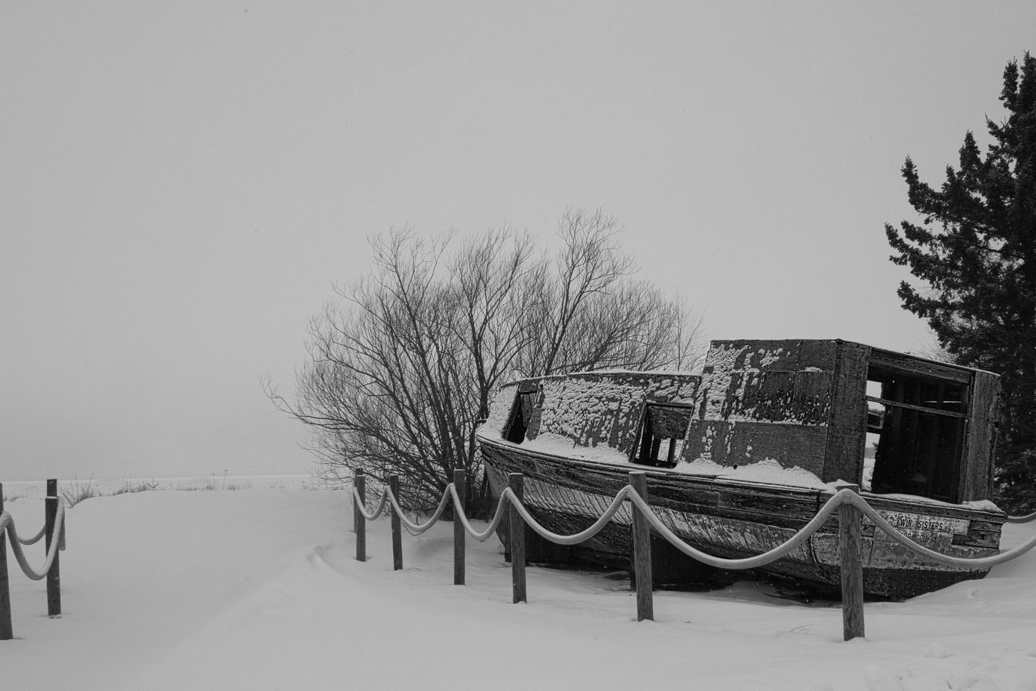 Snow-covered commercial fishing boat resting along a winter shoreline in Northern Wisconsin, captured in black and white.