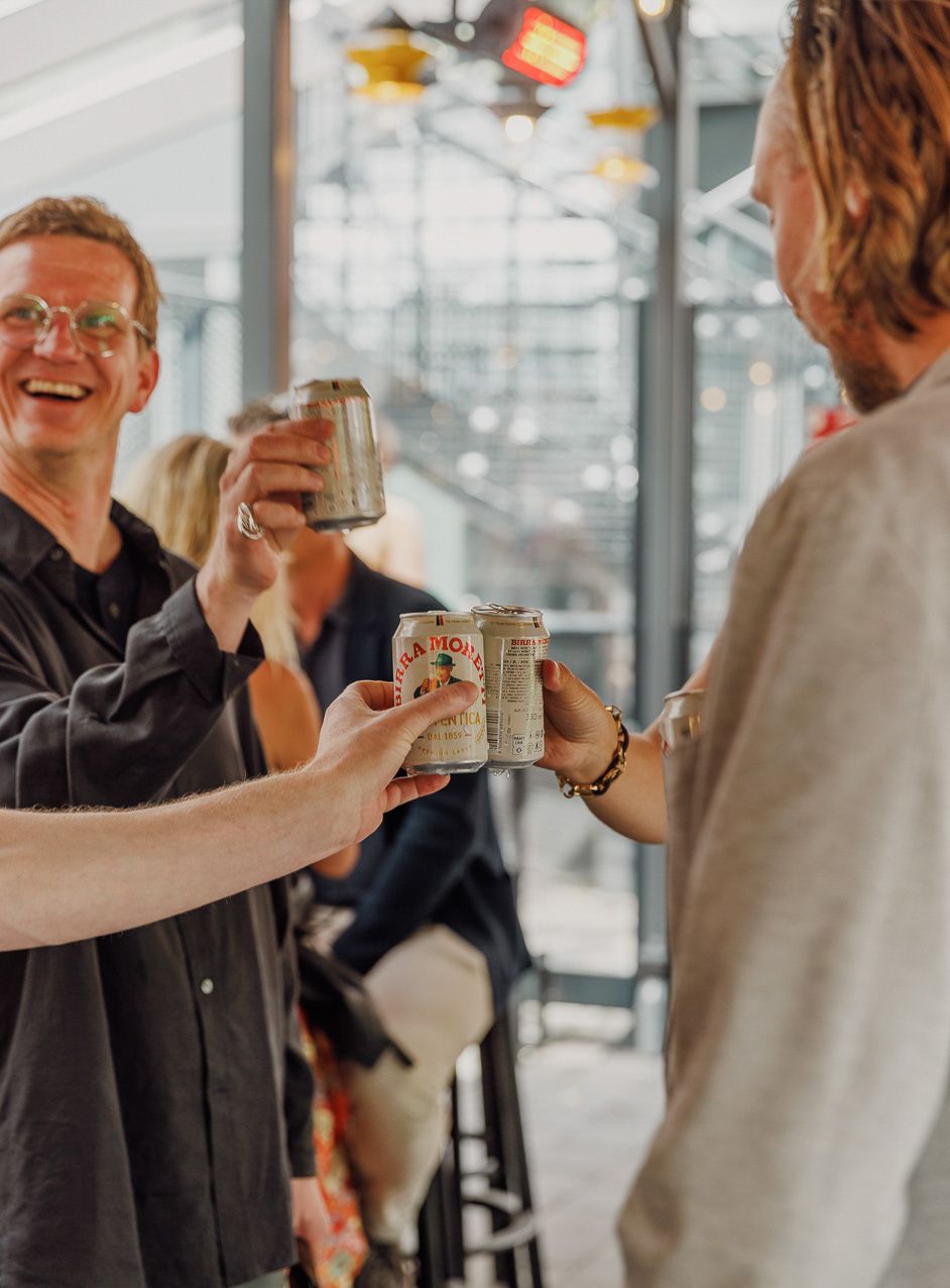 Vänner skålar och skrattar med konserverade drycker i ett ljust modernt kontorsutrymme