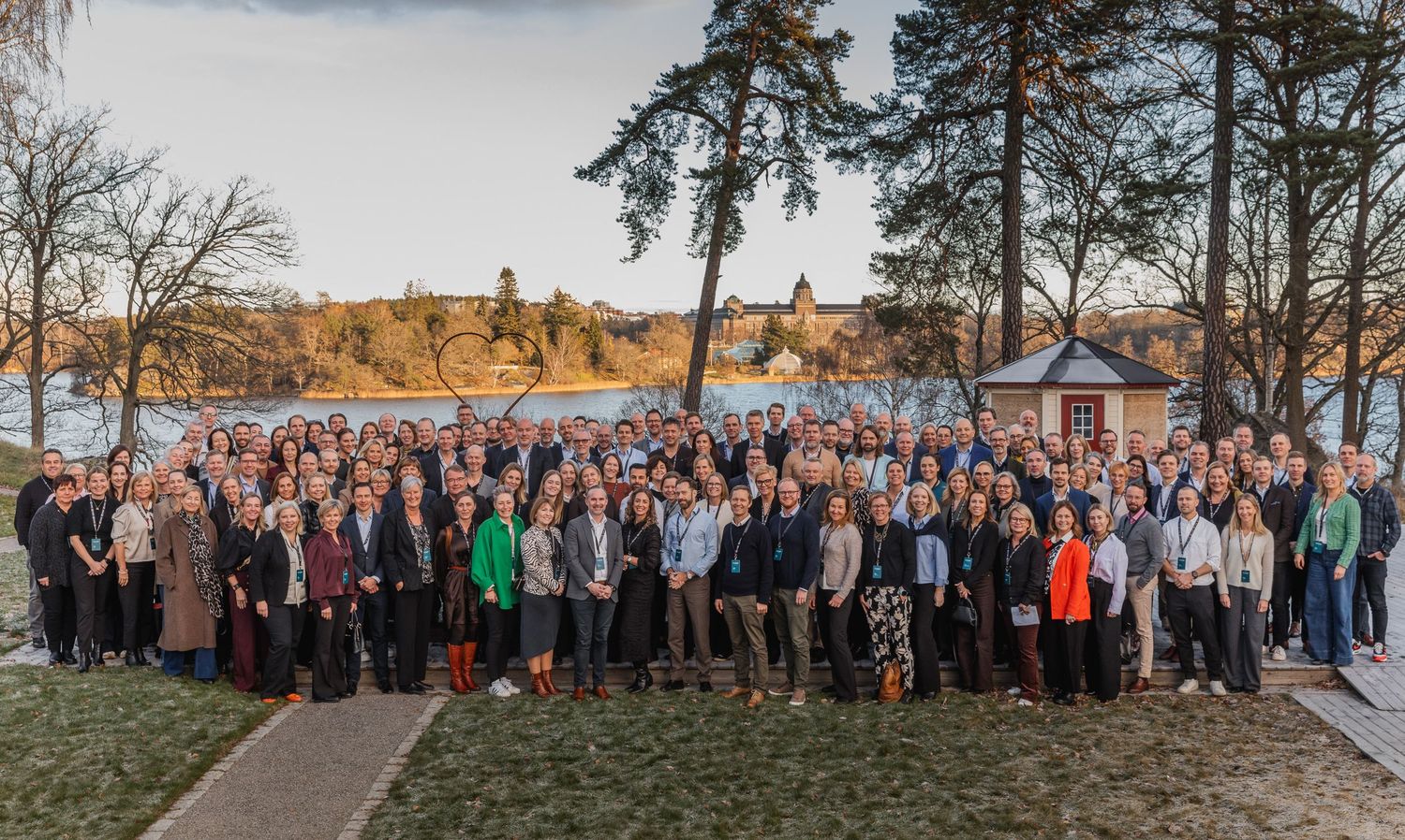 Stor grupp anställda samlades utomhus för ett företagsfoto med träd i bakgrunden