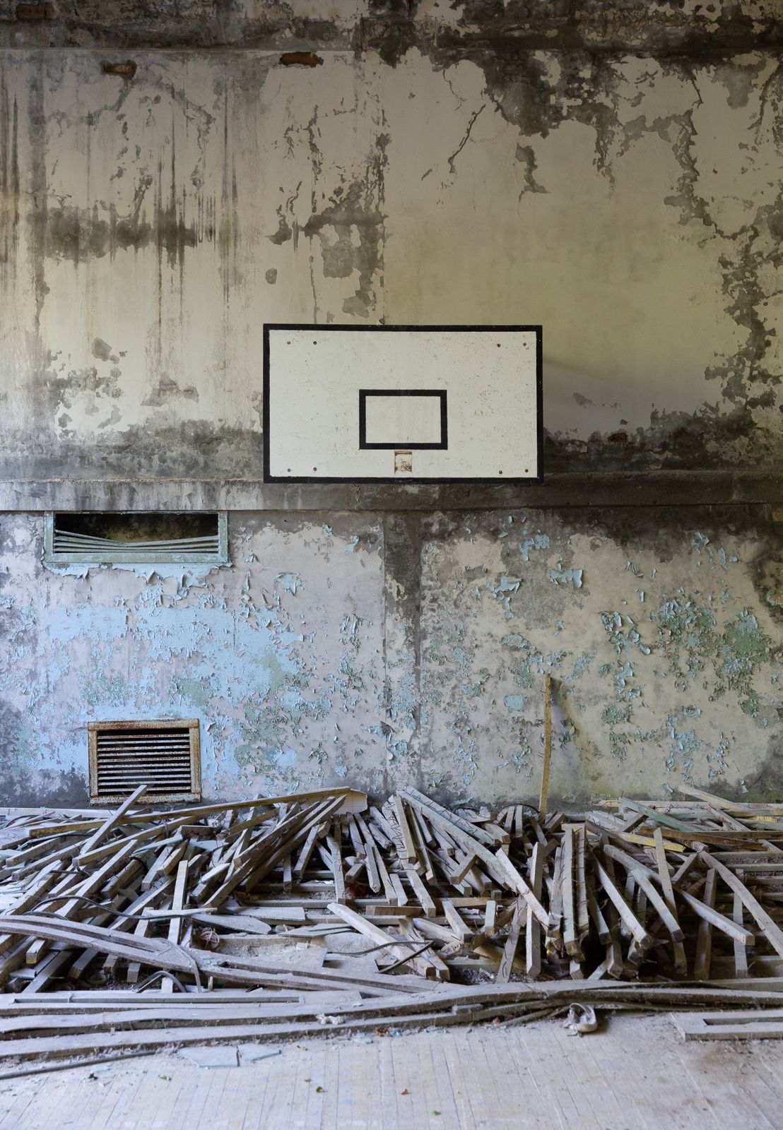 Abandoned interior space with peeling walls and scattered wooden planks on the floor.