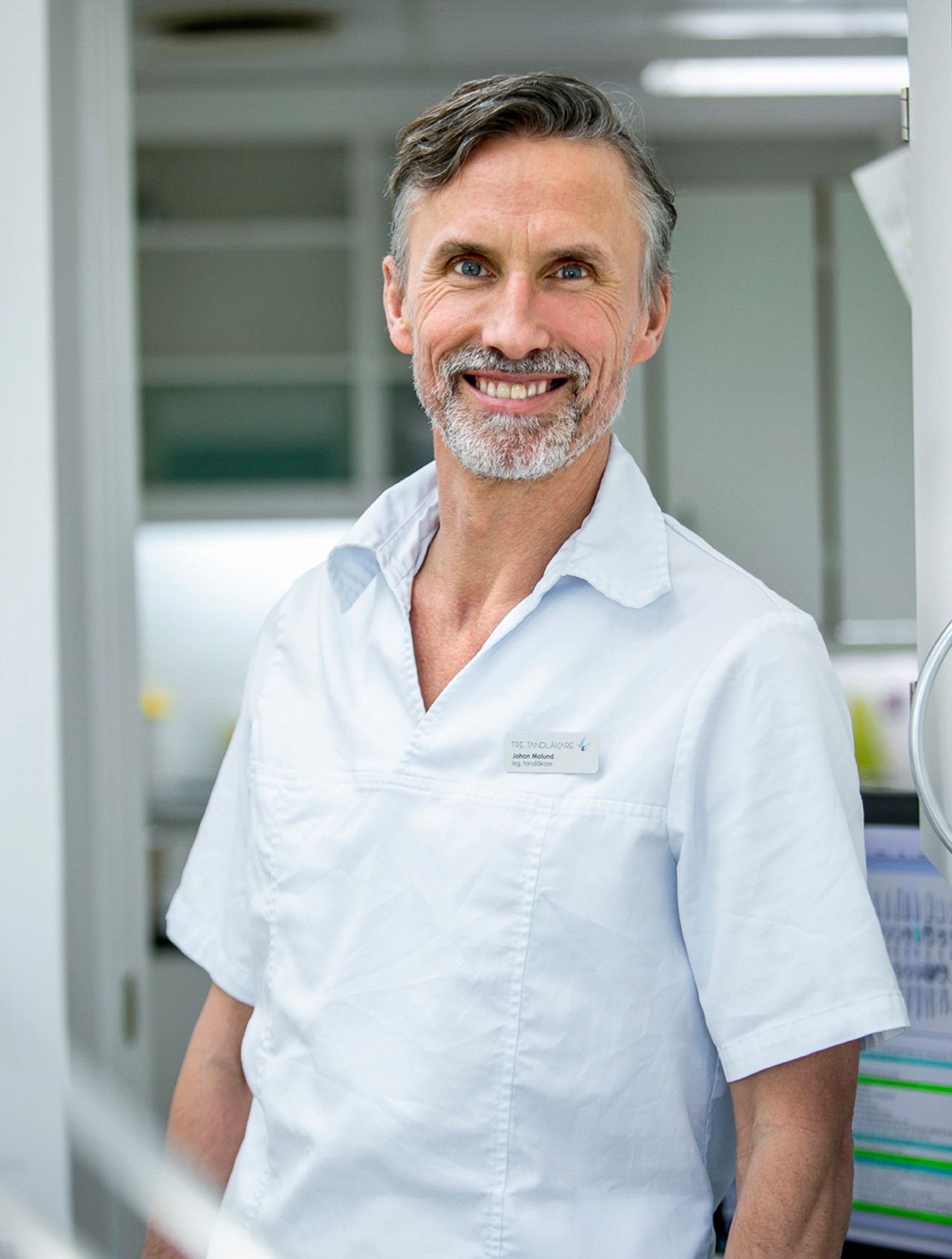 Healthcare professional in white uniform standing in modern medical facility hallway.